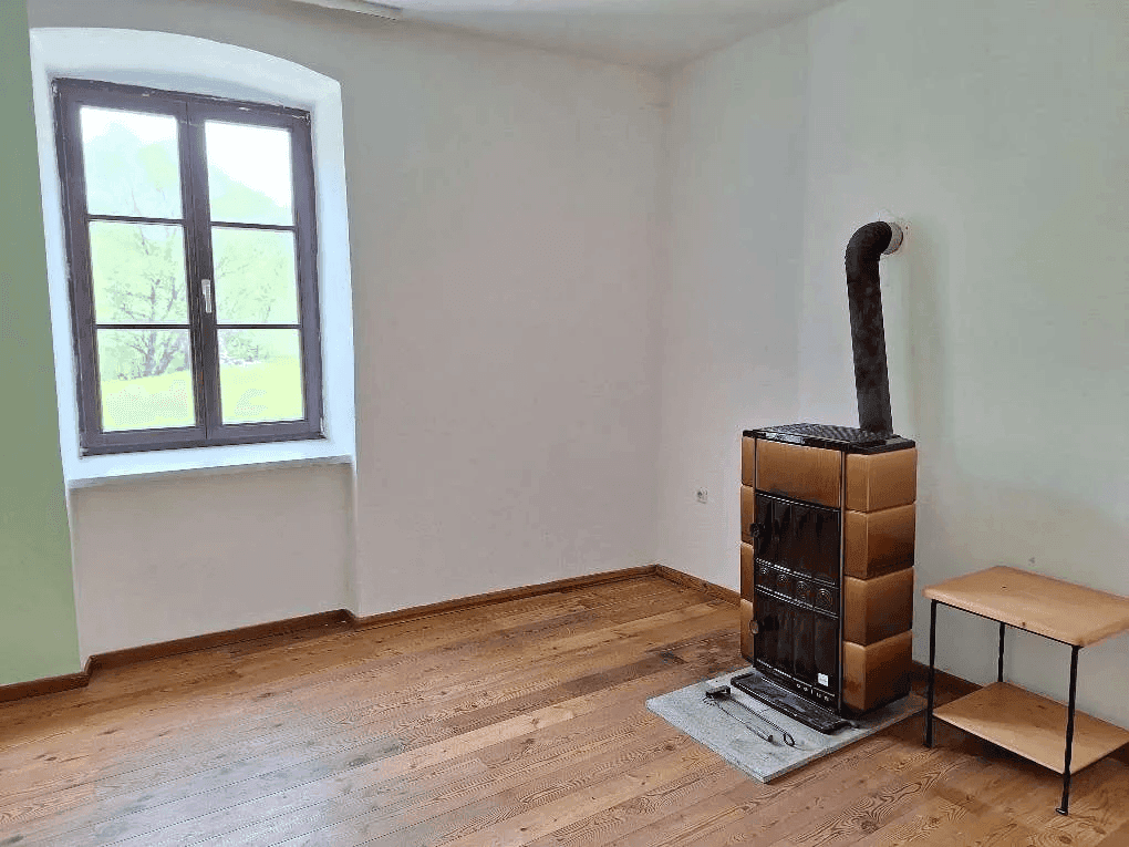 Geräumiges Zimmer mit Holzboden, Kaminofen und einem Fenster mit Blick auf die Landschaft.