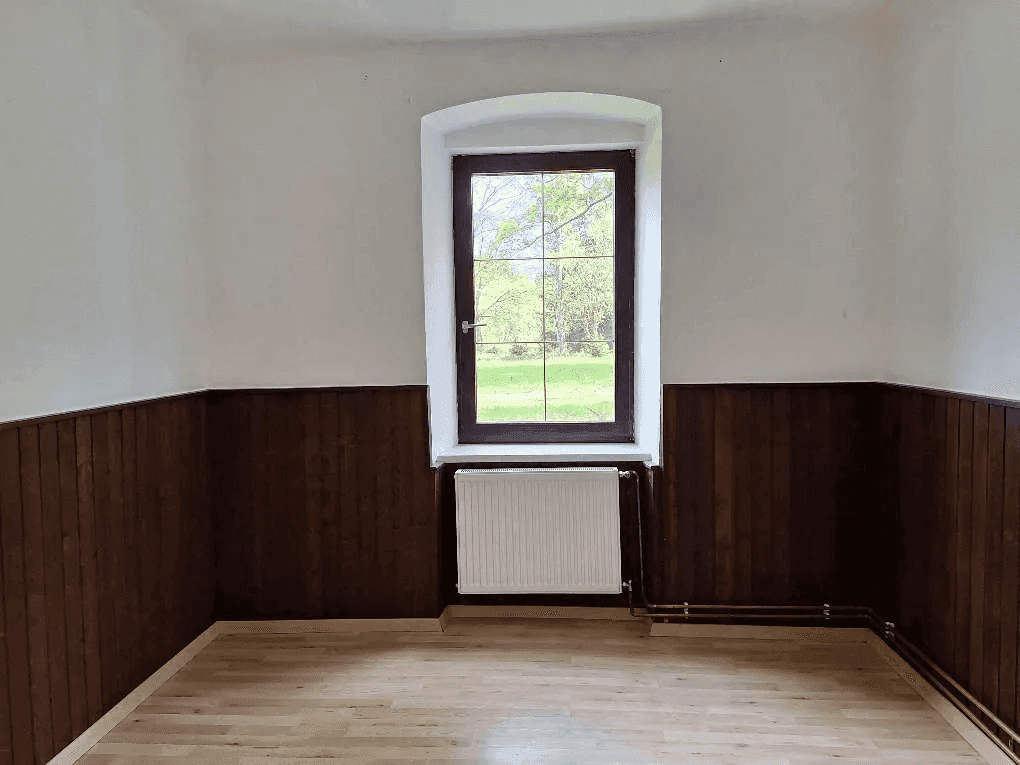 Helles Zimmer mit Holzvertäfelung, Parkettboden und einem Fenster mit Blick ins Grüne.
