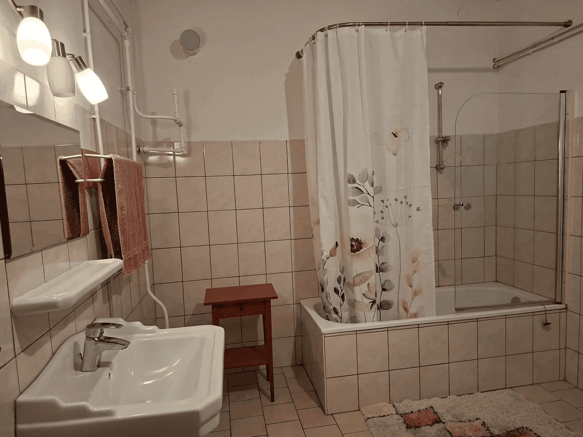 Gefliestes Badezimmer mit Badewanne, Duschvorhang und Waschbecken.