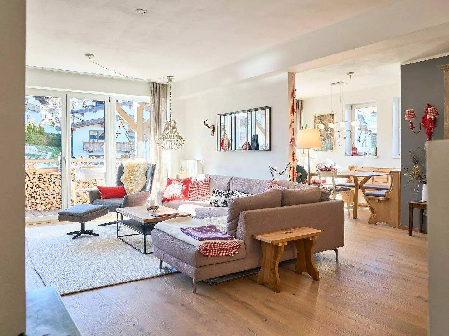 Heller Wohn- und Essbereich mit Holzboden, großem Sofa und Zugang zum Balkon.