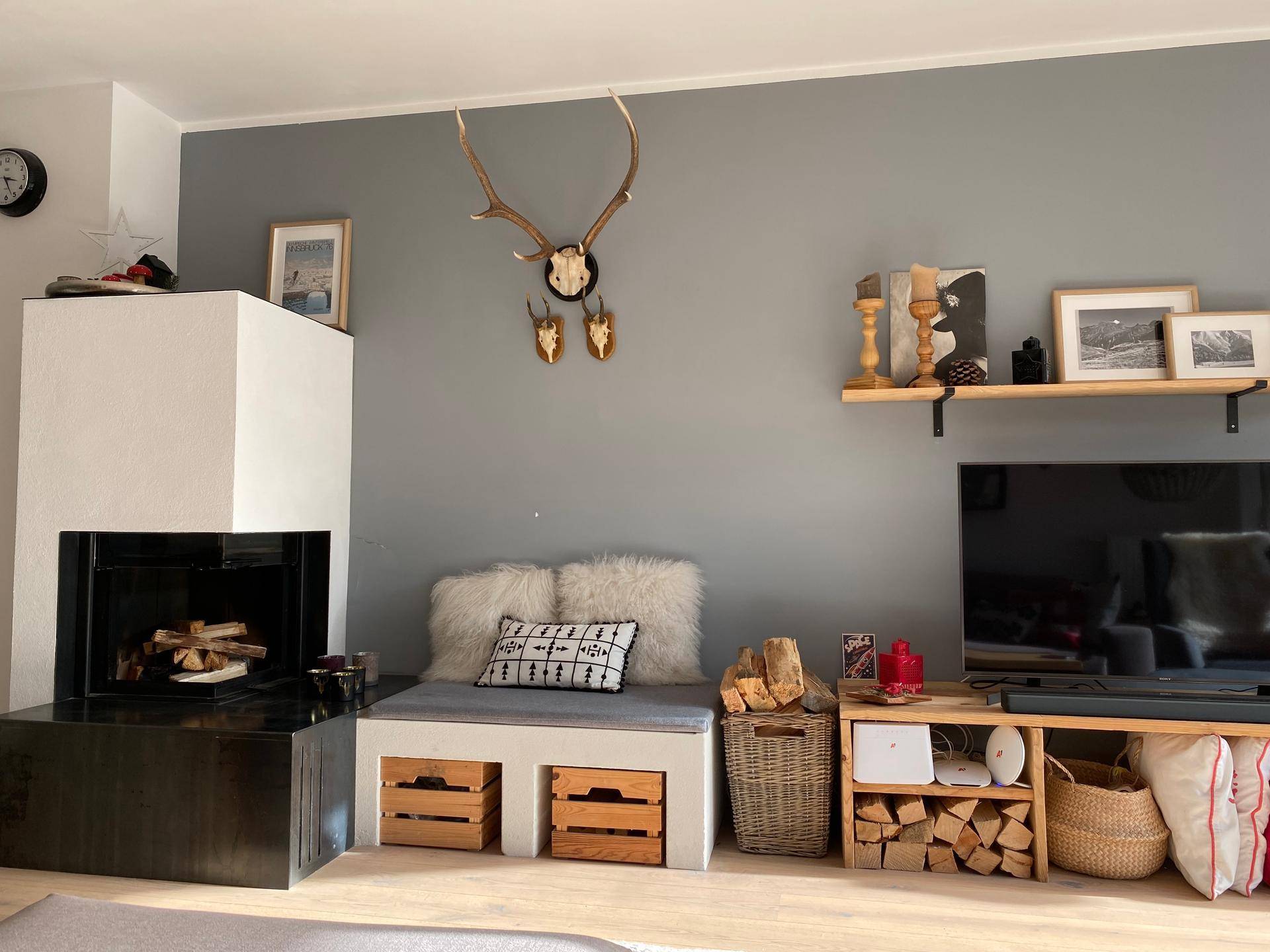 Wohnzimmer mit modernem Kamin, Sitzbank und alpiner Dekoration an der grauen Wand.