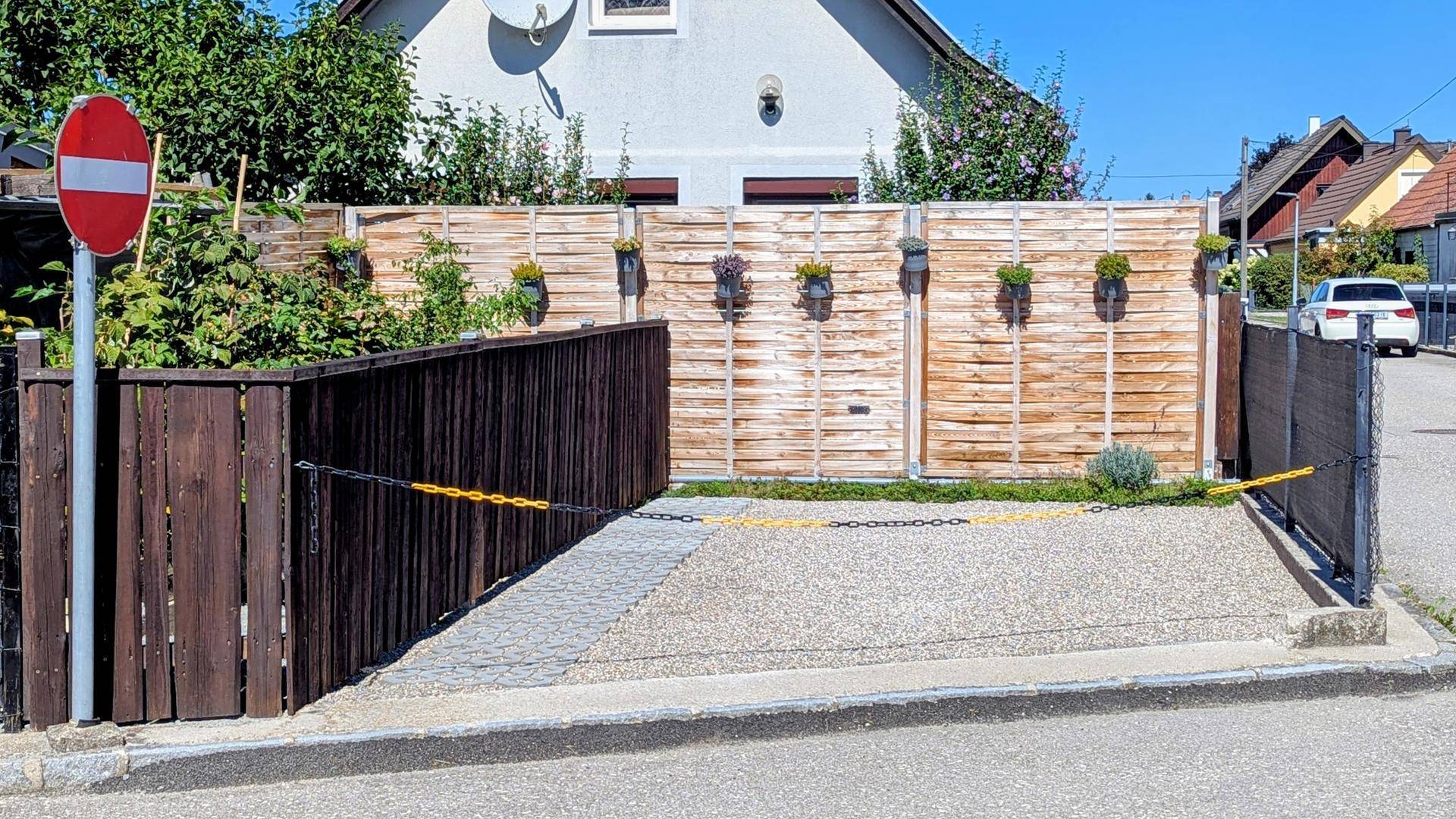 Nahaufnahme eines privaten Stellplatzes mit Kiesbelag, umgeben von einem hohen Holzzaun und einem Stoppschild.