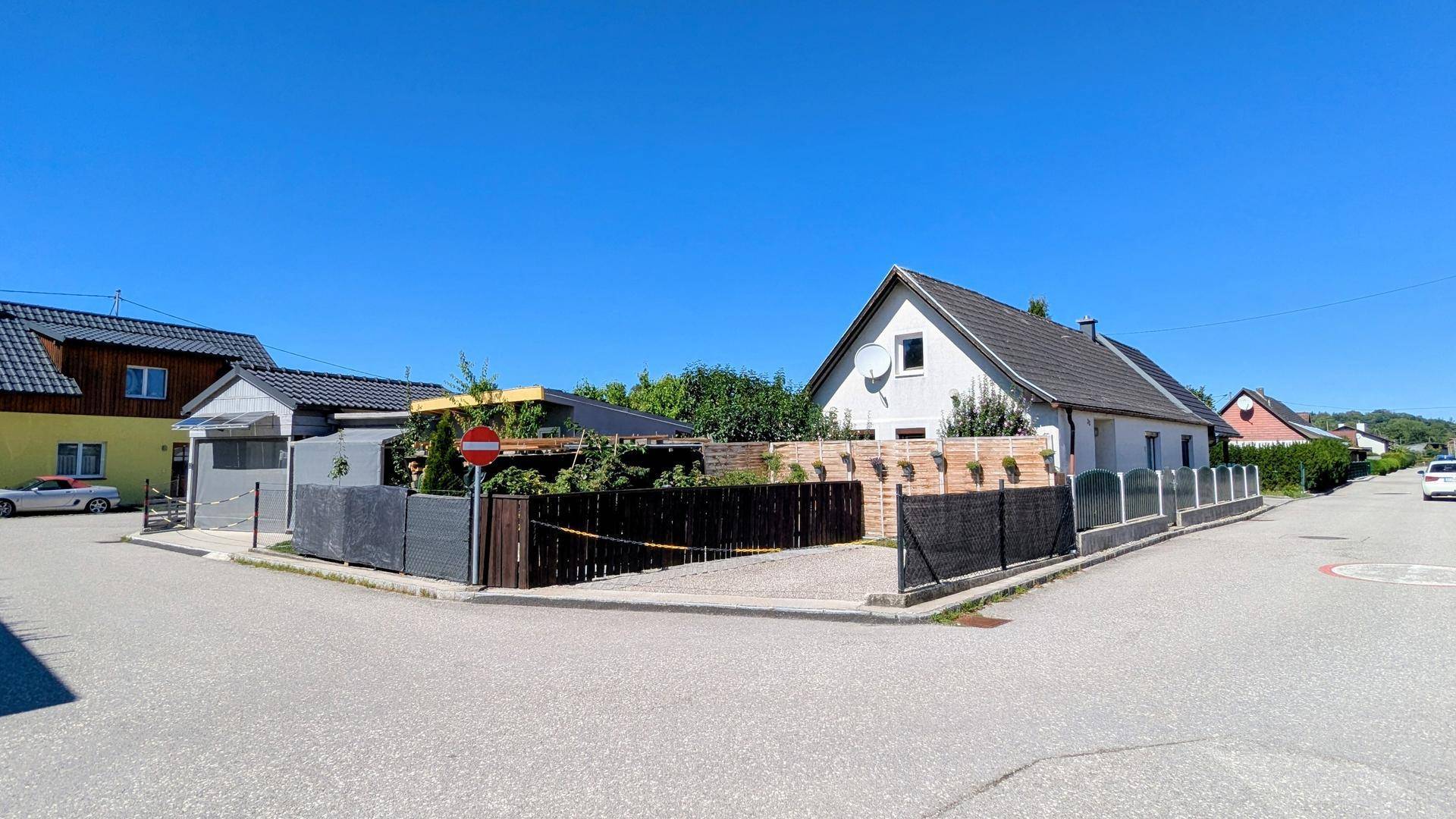 Panoramablick auf eine Wohngegend mit verschiedenen Häusern und einem sonnigen Parkplatz an der Straße.