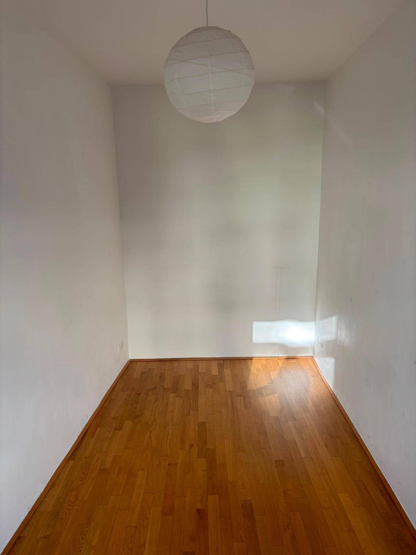 Leerer Raum mit Holzfußboden und weißen Wänden, durchflutet von natürlichem Sonnenlicht.