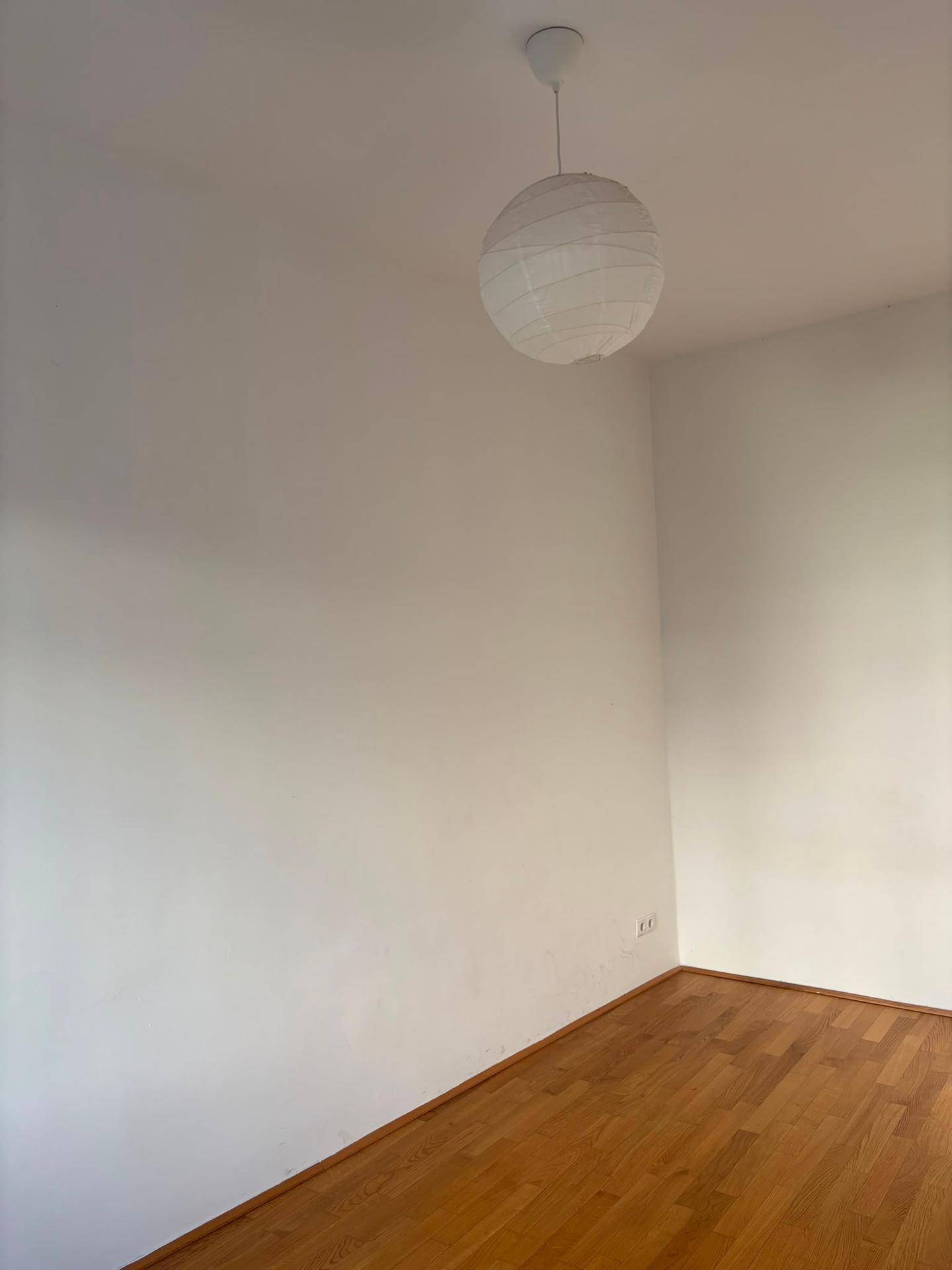 Leerer Raum mit weißen Wänden, Holzfußboden und einer schlichten Deckenleuchte.