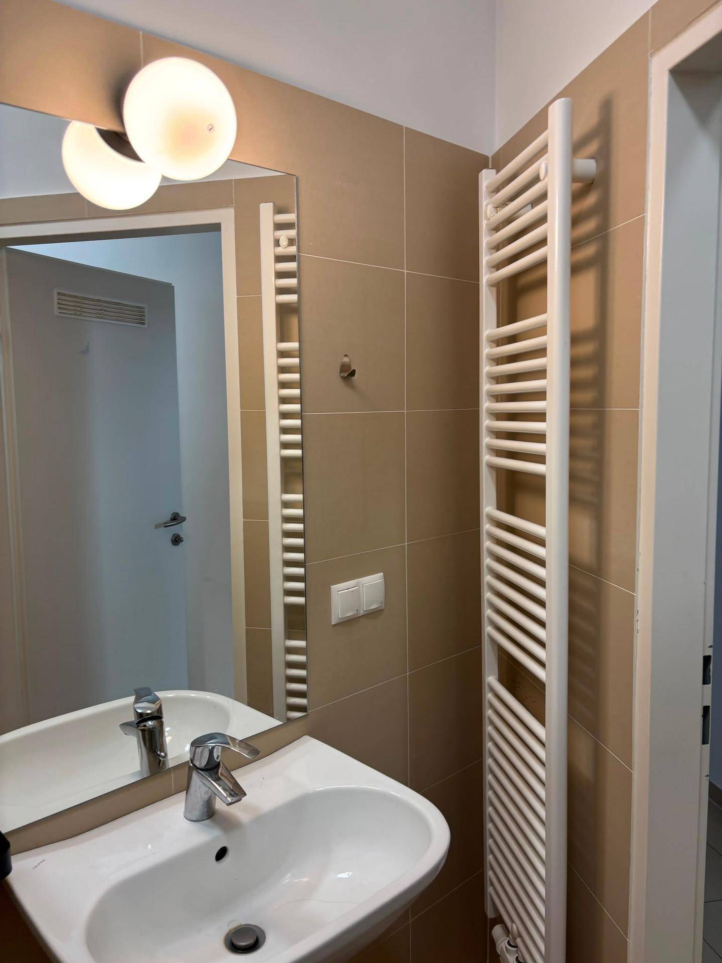 Badezimmer mit Waschbecken, Spiegel, beigen Fliesen und einem beheizten Handtuchhalter.