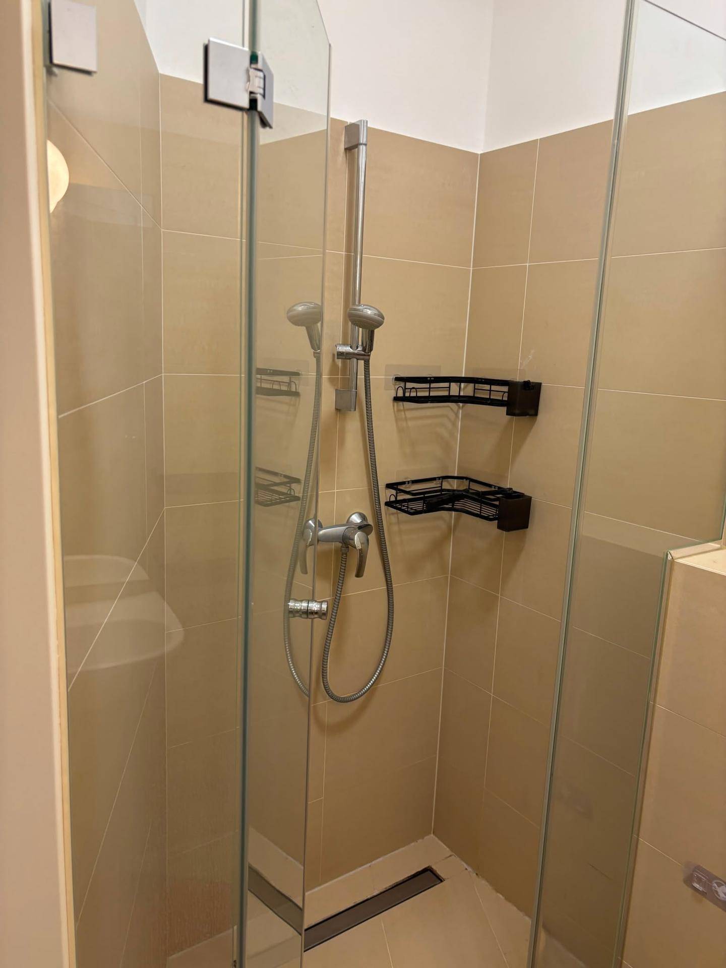 Duschbereich mit beigen Fliesen und Glasabtrennung in einem modernen Badezimmer.