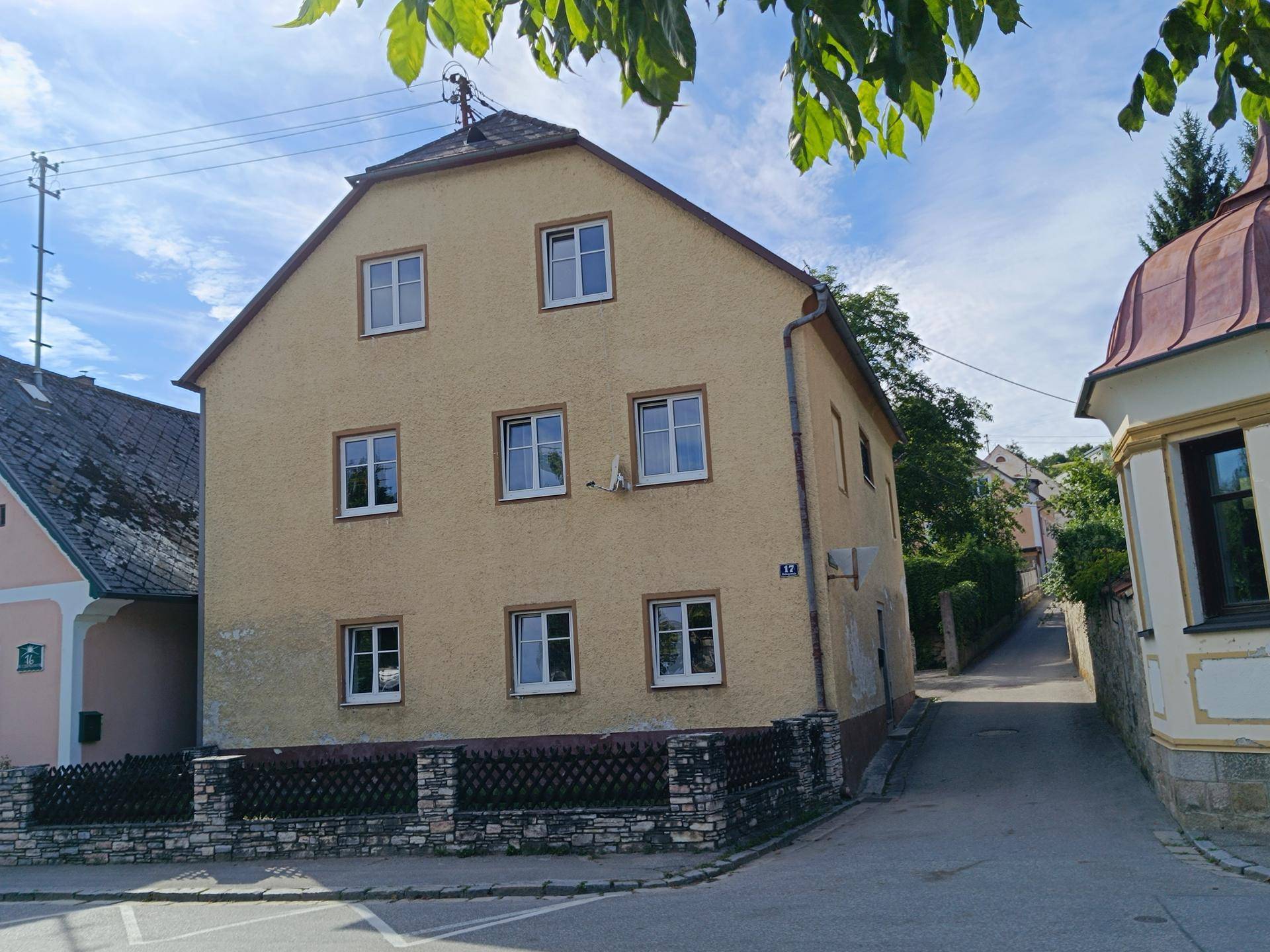 Ansicht des gelben Wohnhauses mit mehreren Fenstern und einem kleinen Zaun an der Straßenecke.