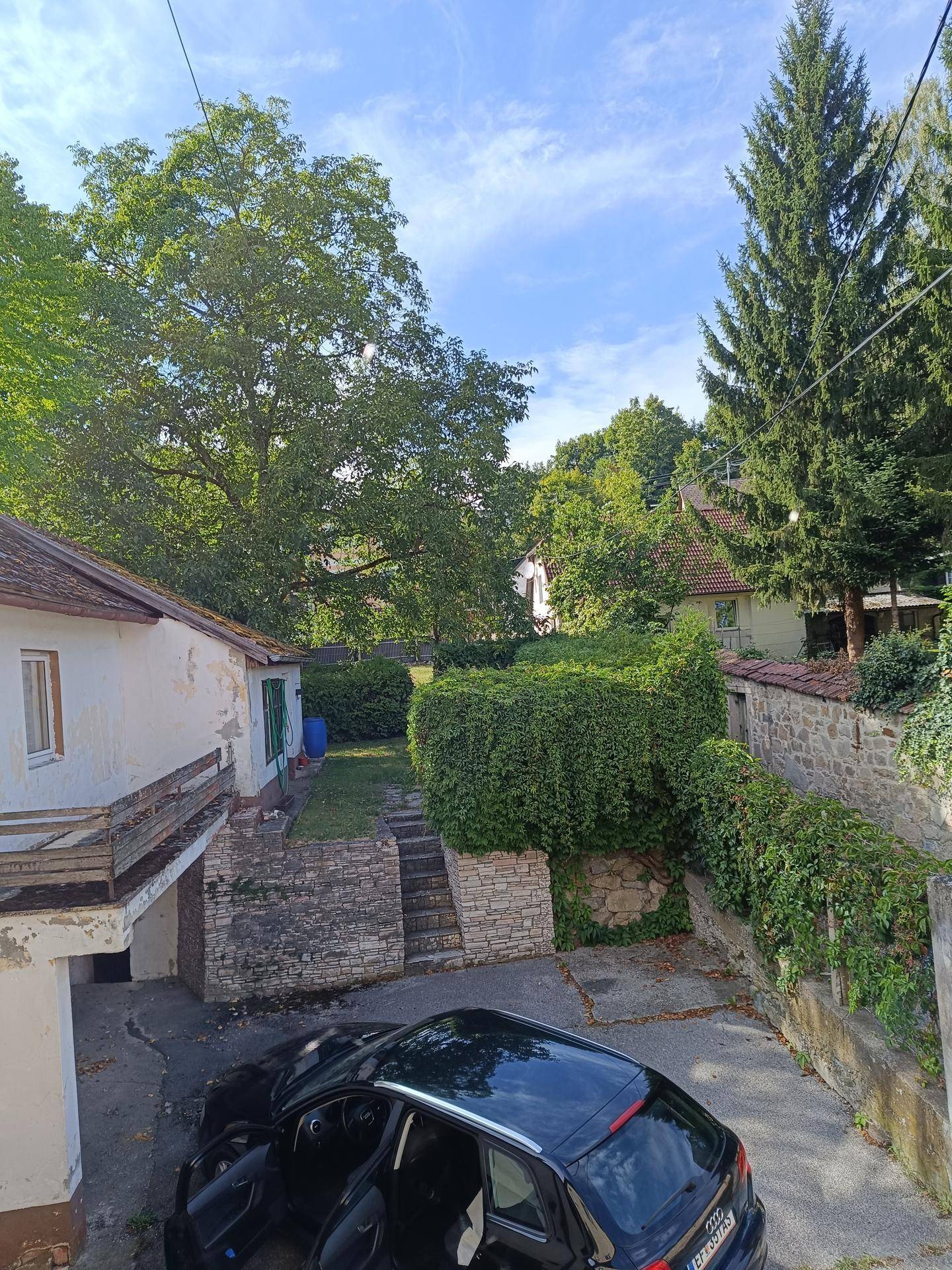 Hinterhofbereich mit einem geparkten Auto, umgeben von alten Gebäuden, Mauern und üppigem Grün.
