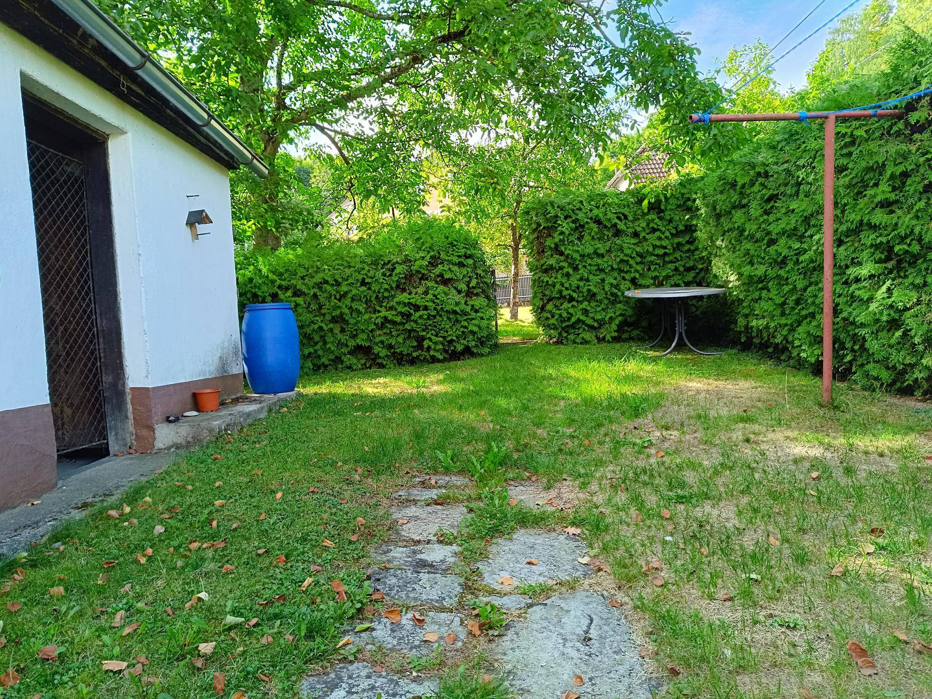 Gepflegter Gartenbereich mit Rasenfläche, Hecken, einem kleinen Schuppen und einem Gartentisch.
