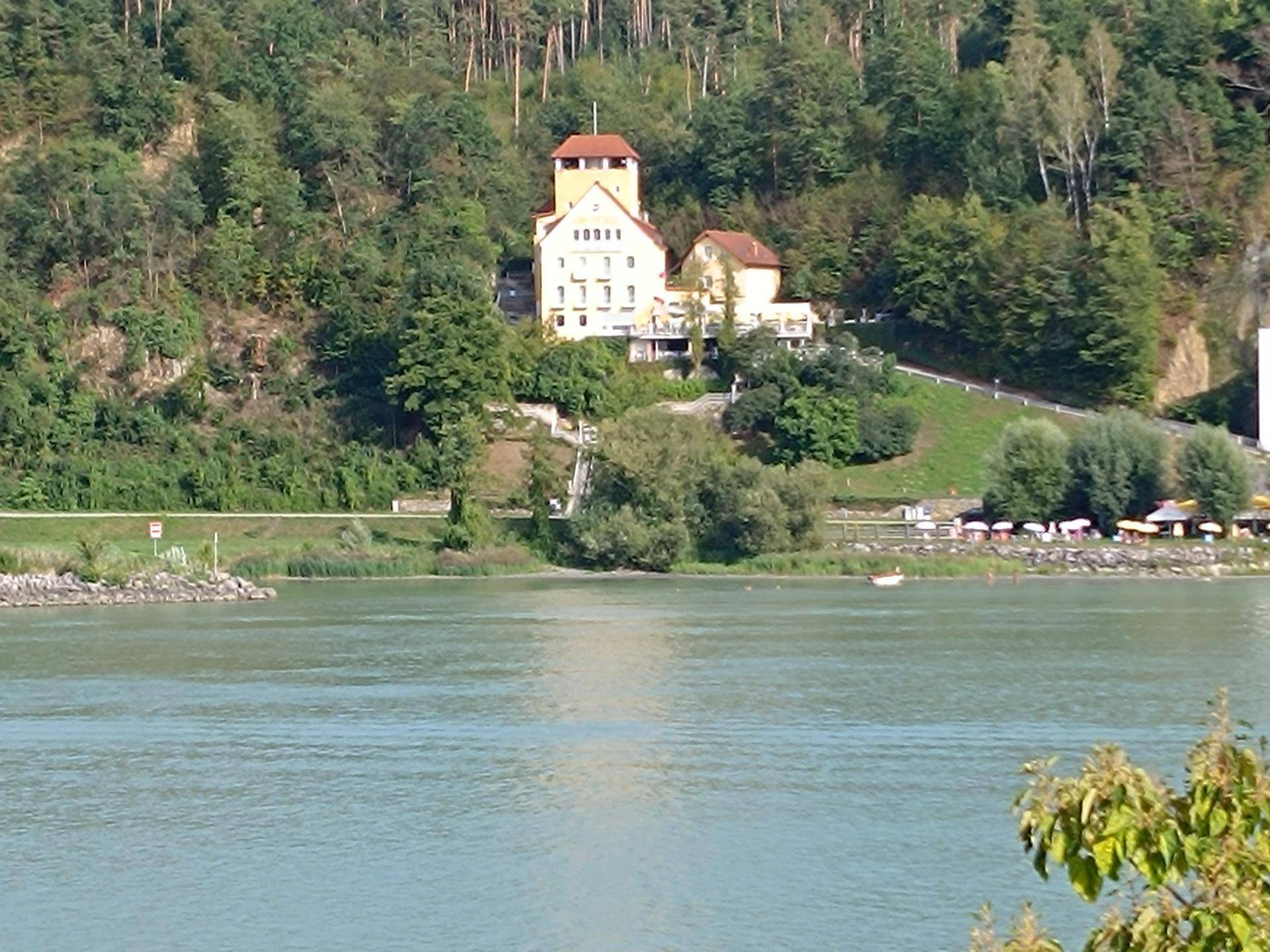 Detaillierterer Blick auf das historische Gebäude auf dem Hügel, umgeben von üppiger Vegetation und dem See.