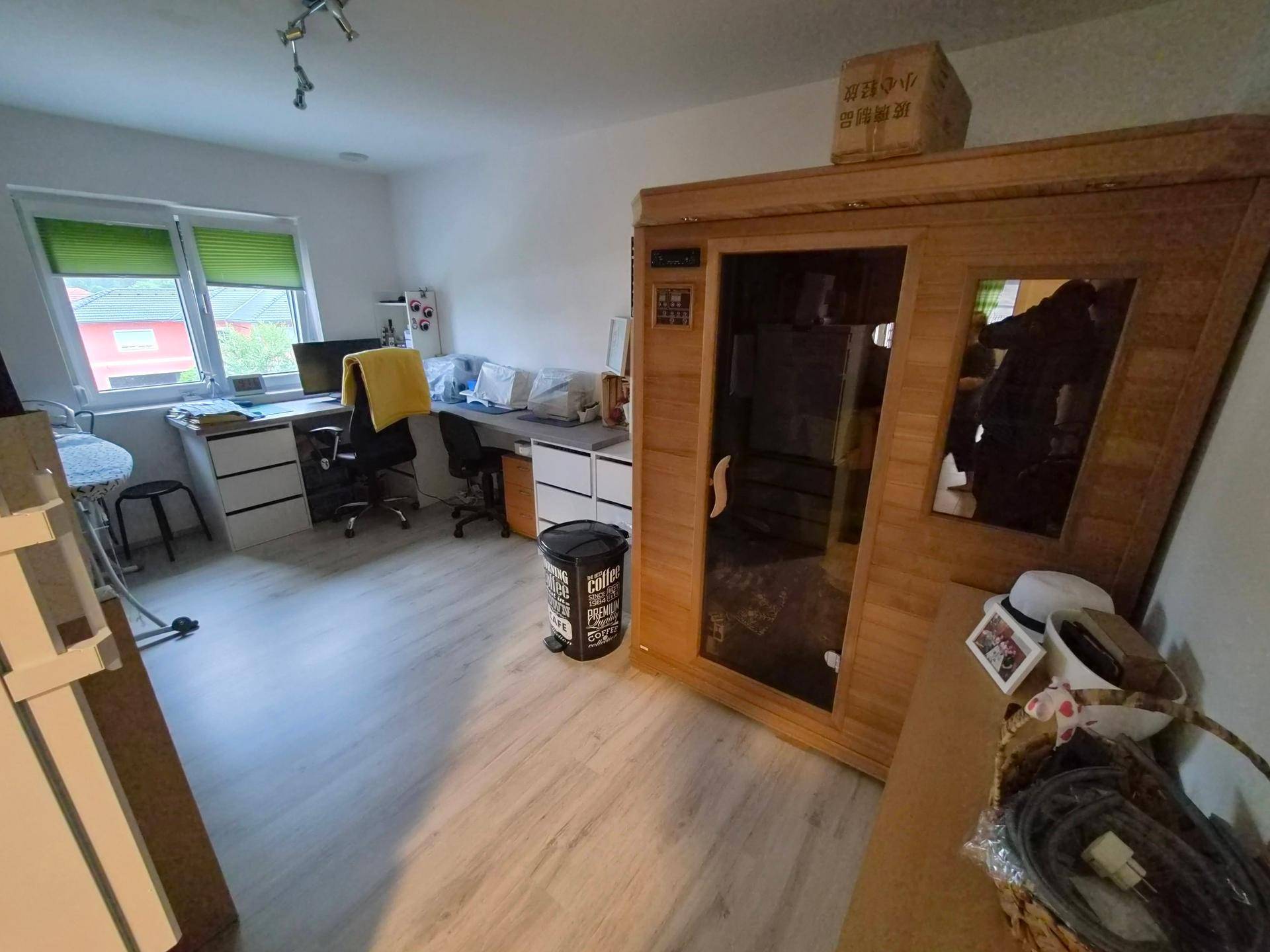 Zimmer mit Schreibtisch, Laminatboden und einer sichtbaren Sauna für Entspannung.