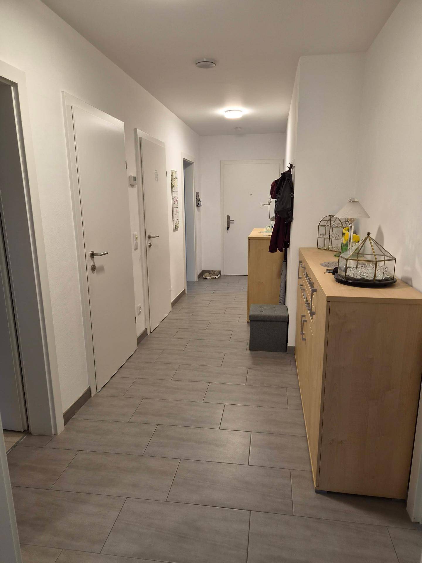 Einladender Flur mit Fliesenboden, weißen Türen und Holzkommode.