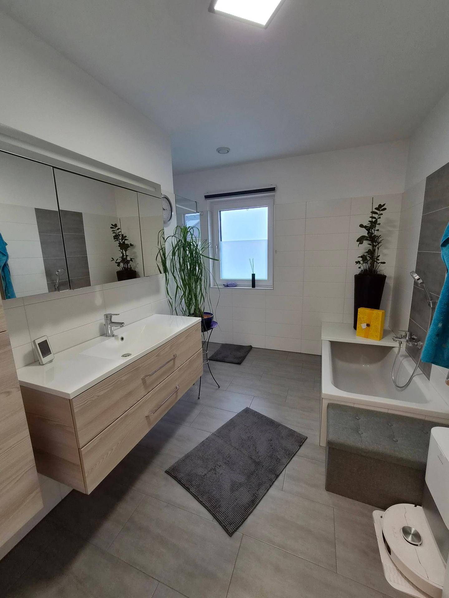 Modernes Badezimmer mit Einzelwaschbecken, Badewanne und Fenster für Tageslicht.