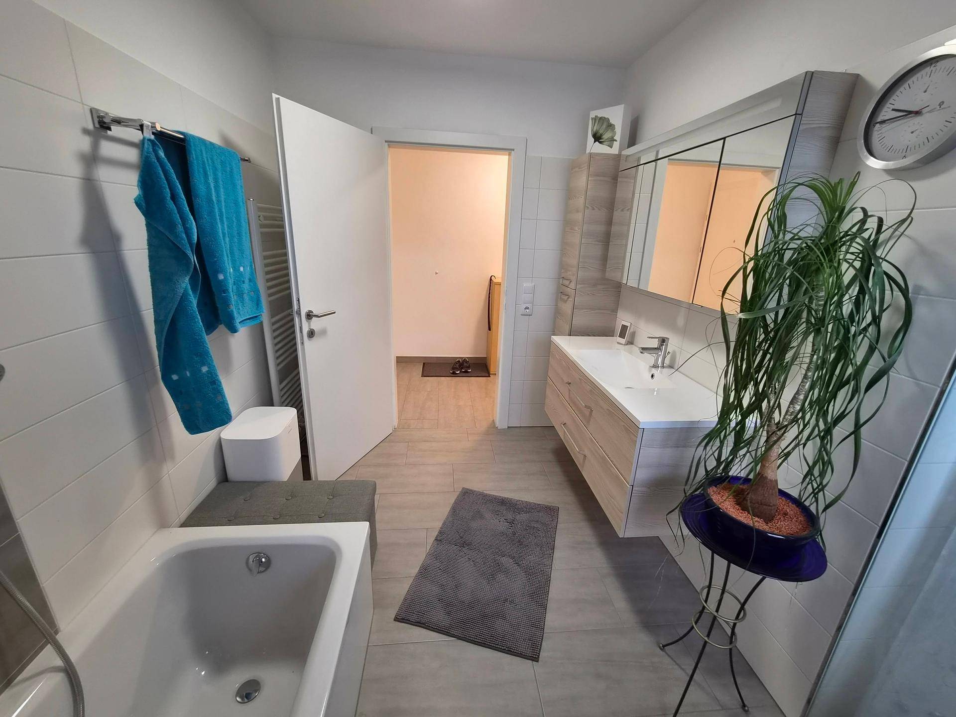 Helles Badezimmer mit Badewanne, Einzelwaschbecken, Spiegelschrank und Handtuchheizkörper.