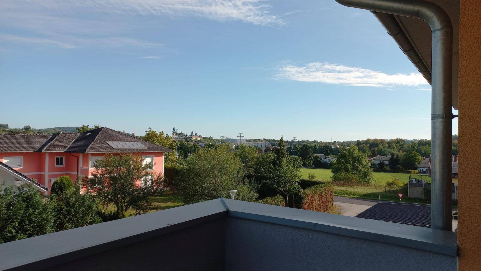 Weitläufiger Blick über grüne Landschaft und Dächer von einem Balkon.