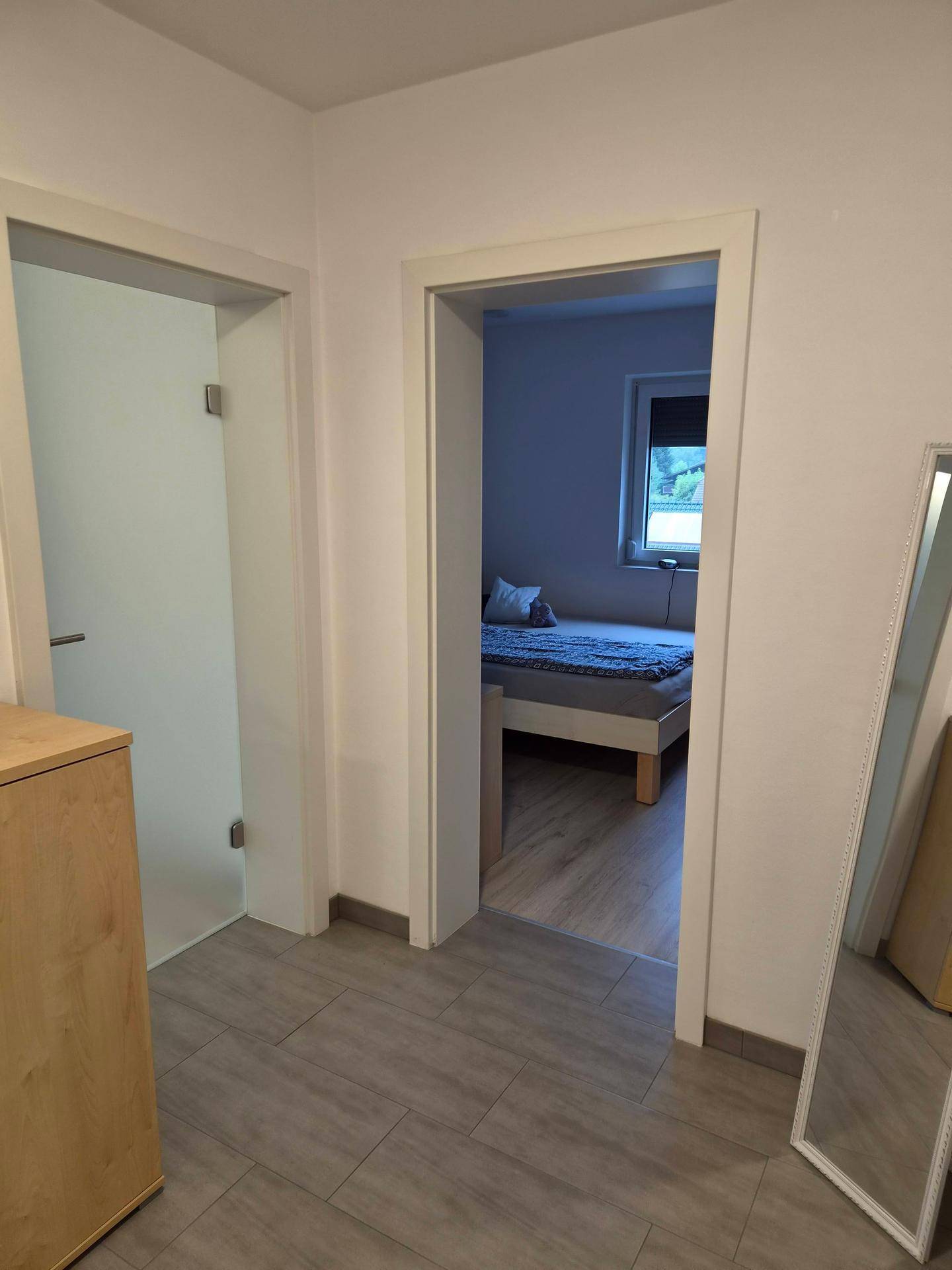 Flur mit Fliesenboden und Blick in ein angrenzendes Schlafzimmer.