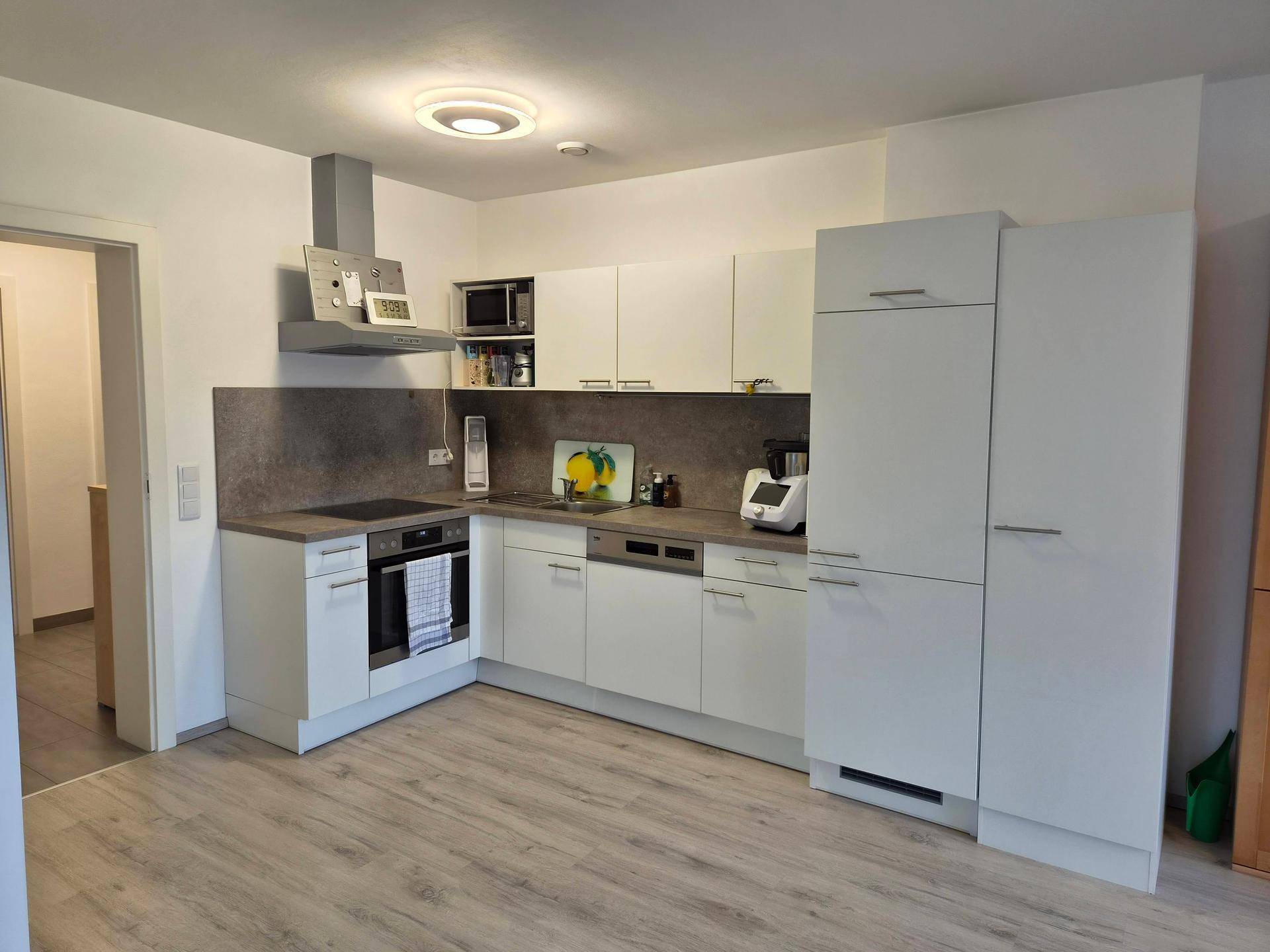 Moderne Einbauküche mit weißen Schränken, Induktionskochfeld und integrierten Geräten.