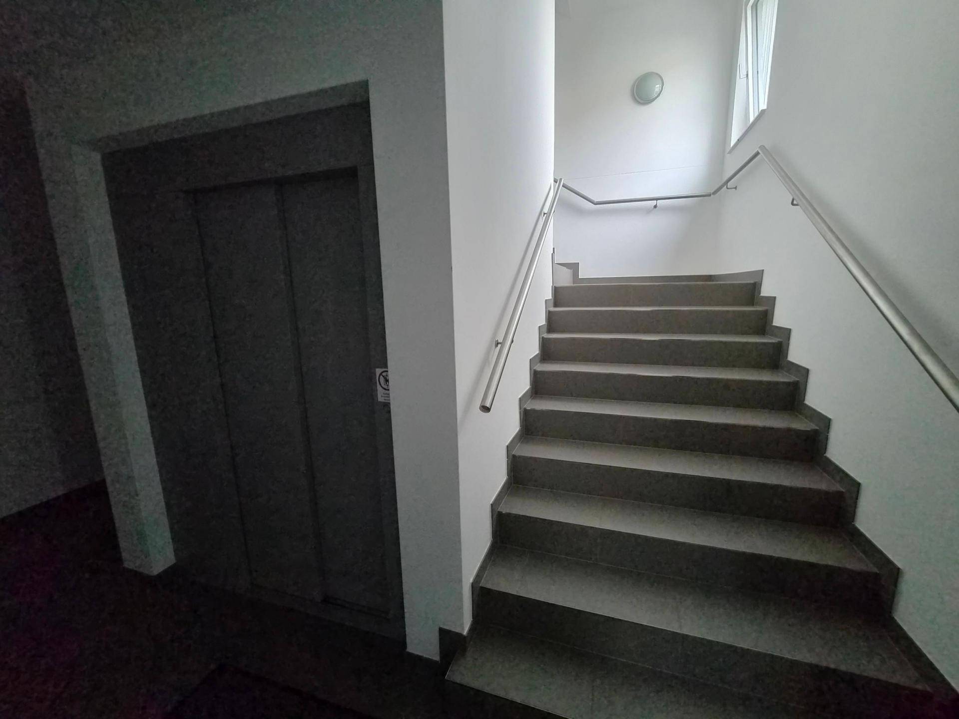 Helles Treppenhaus mit robustem Handlauf und Aufzug in einem modernen Gebäude.