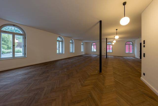 Großer, leerer Raum mit elegantem Fischgrätparkett, hohen Decken und vielen Bogenfenstern.