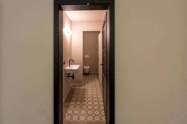 Modernes Gäste-WC mit gemusterten Fliesen, minimalistischem Waschbecken und dunklem Türrahmen.