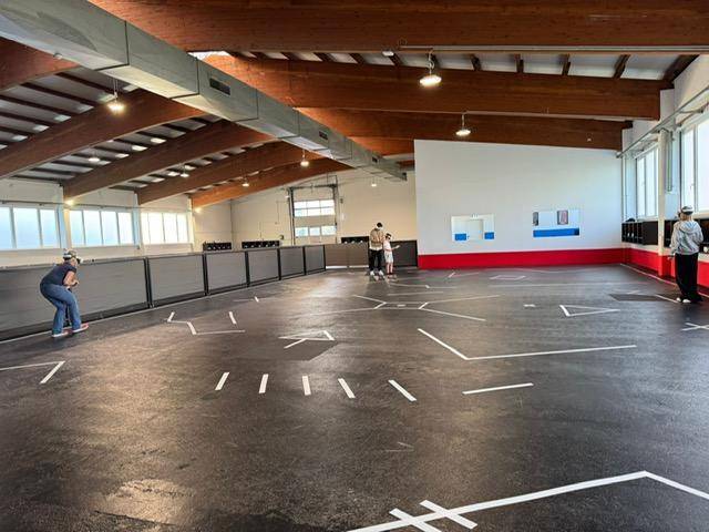 Geräumige Halle mit sichtbaren Holzbalken, viel Tageslicht und einem funktionalen Bodenbelag.