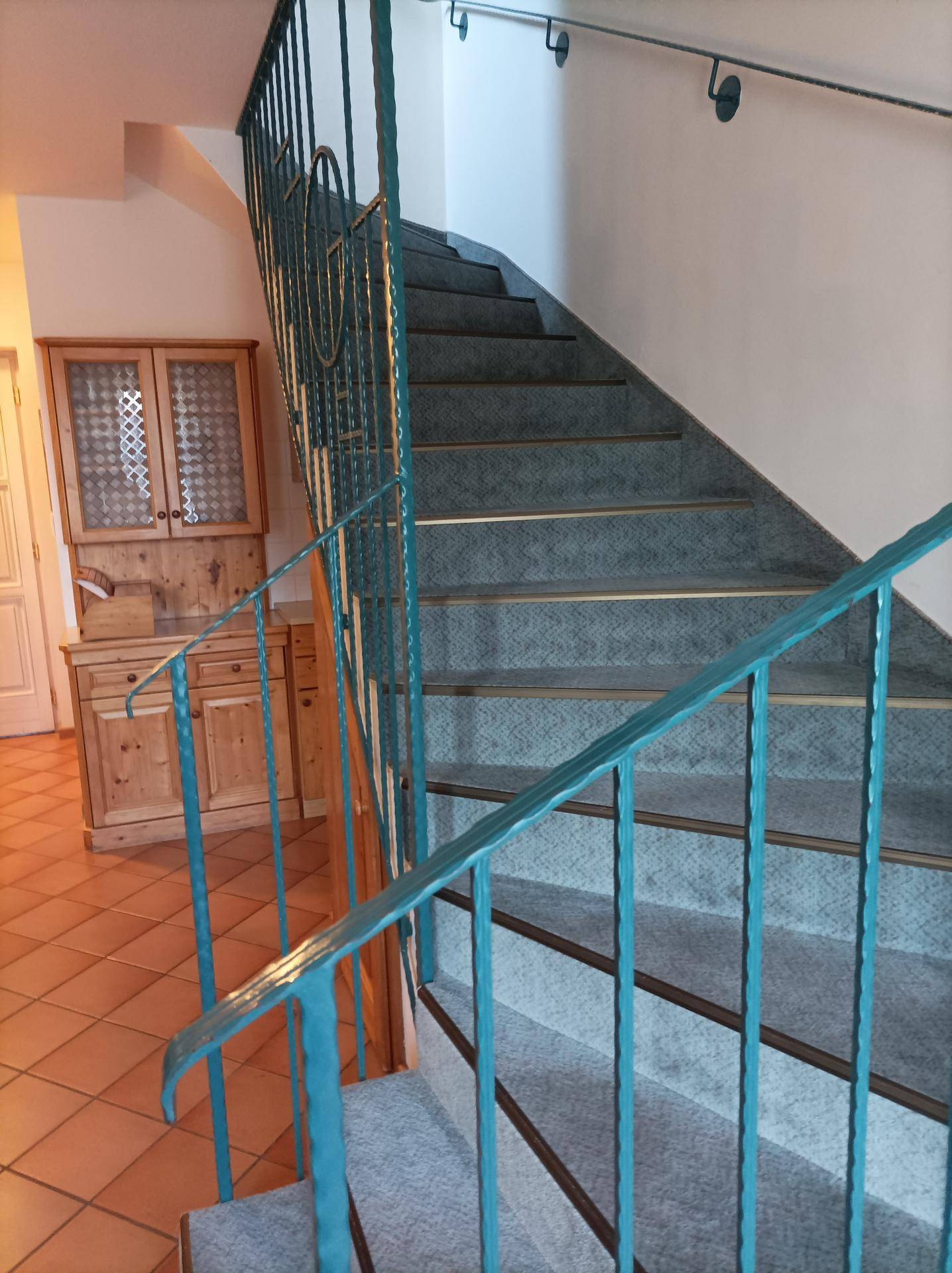 Treppenhaus mit Teppichstufen und einem auffälligen grünen Metallgeländer in traditionellem Stil.