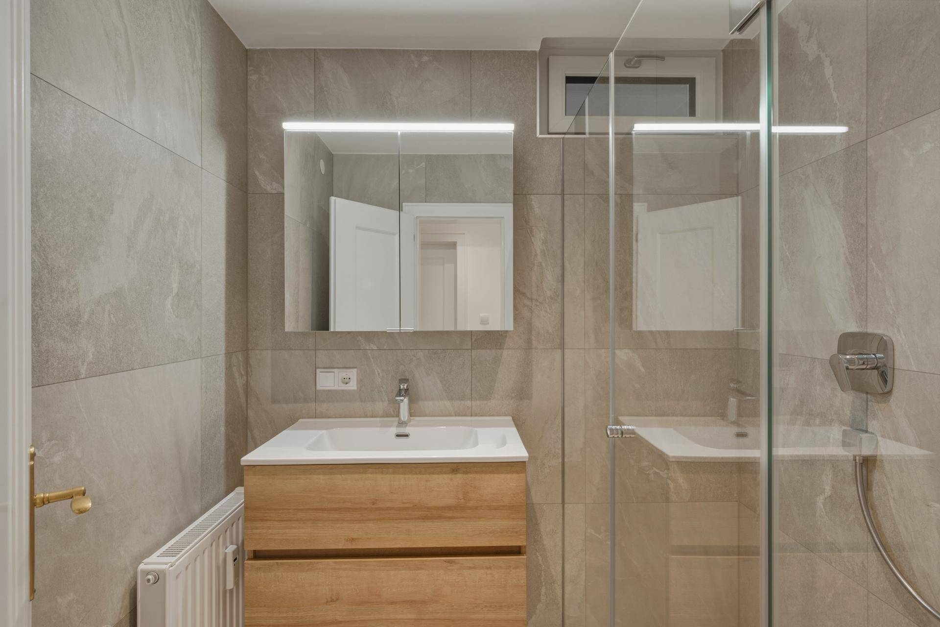 Modernes Badezimmer mit grauen Fliesen, Holzwaschtisch und begehbarer Dusche.