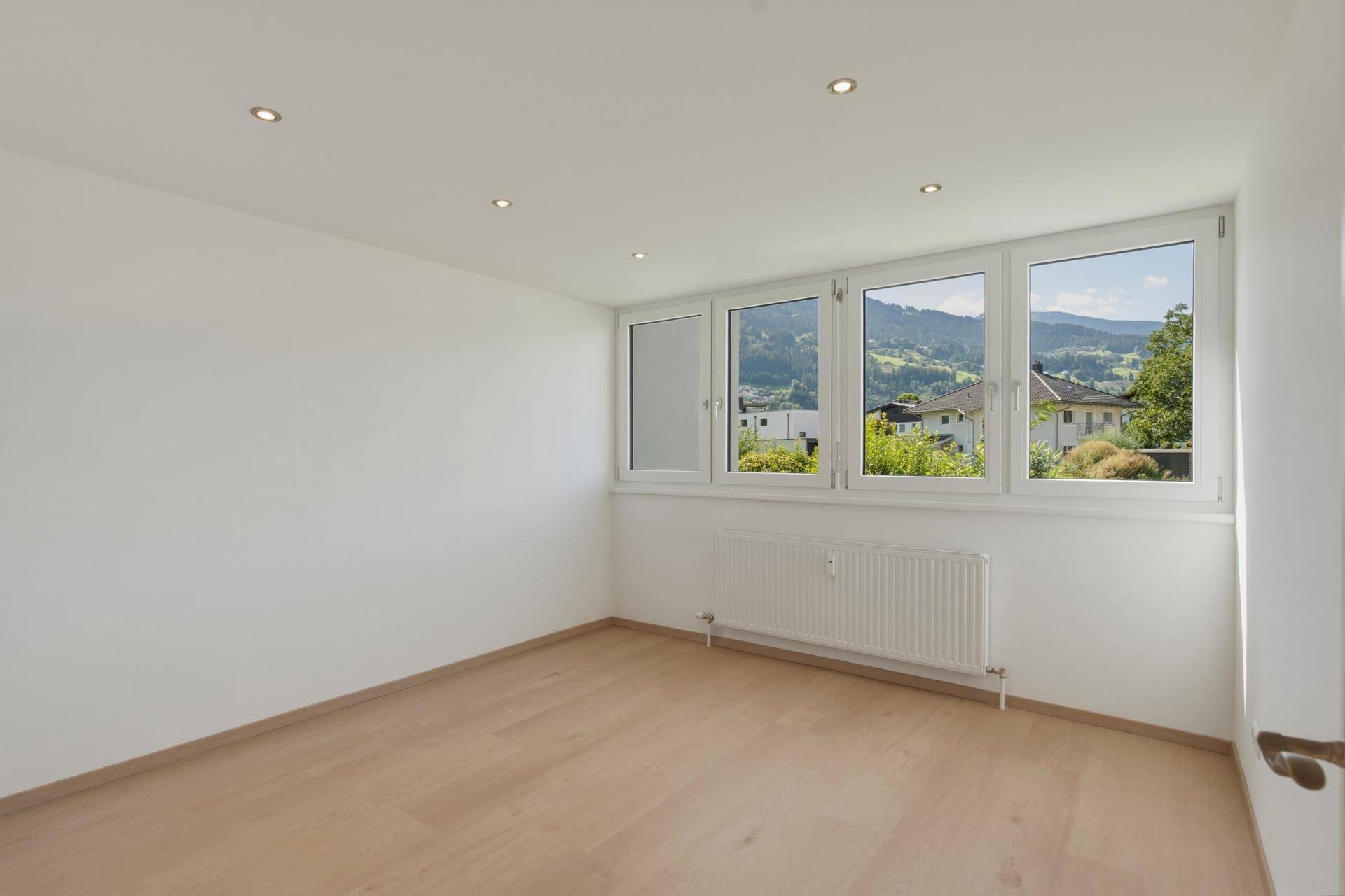 Helles Zimmer mit Holzboden und Panoramafenstern mit Bergblick.