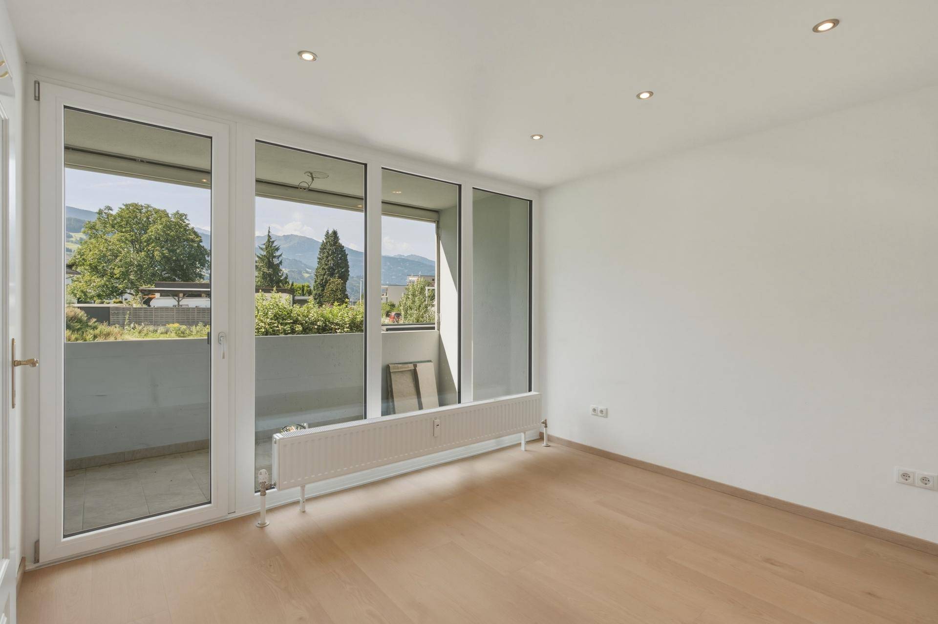 Geräumiges Zimmer mit Holzboden und Zugang zu einem Balkon mit Bergblick.