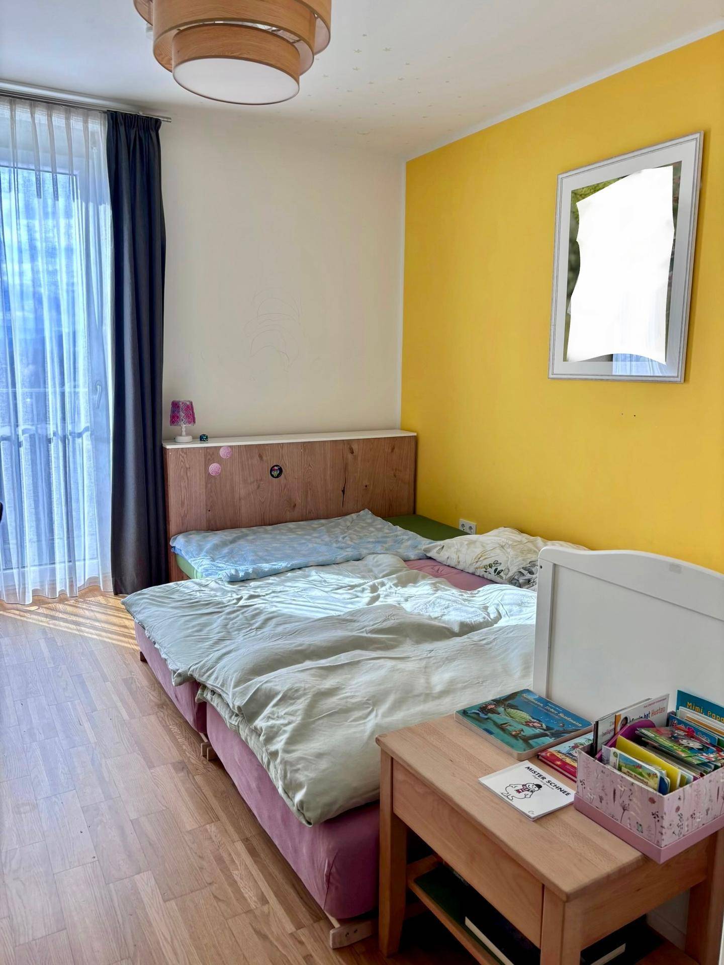 Schlafzimmer mit Doppelbett, Holzkopfteil und einer sonnigen gelben Akzentwand.