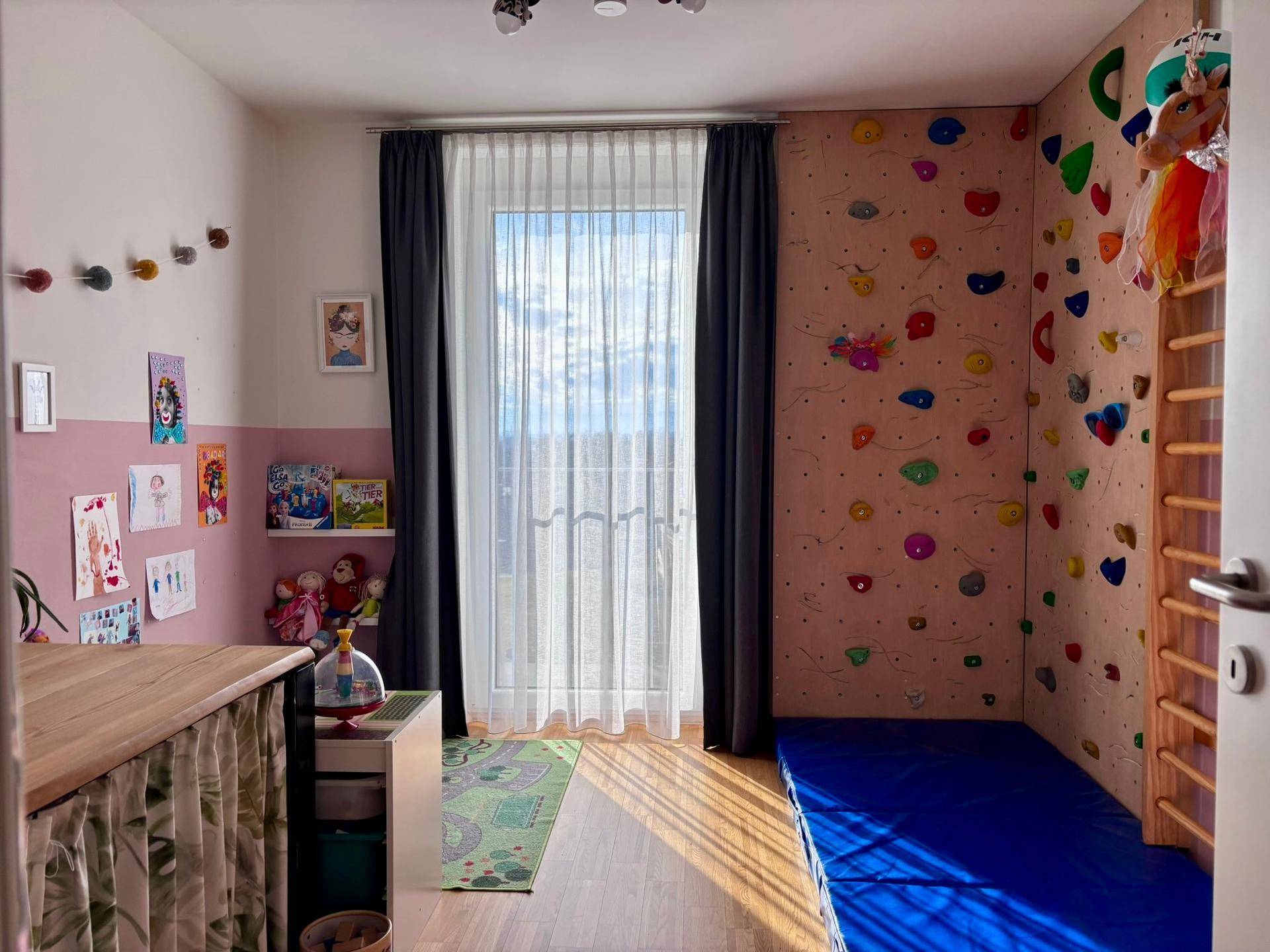 Kinderzimmer mit Kletterwand, rosa Akzentwand und viel Tageslicht durch das Fenster.