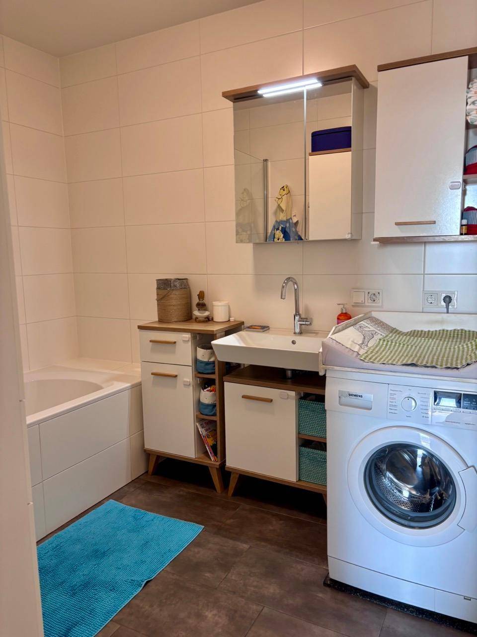 Badezimmer mit Badewanne, Waschbecken, Spiegelschrank und integrierter Waschmaschine.
