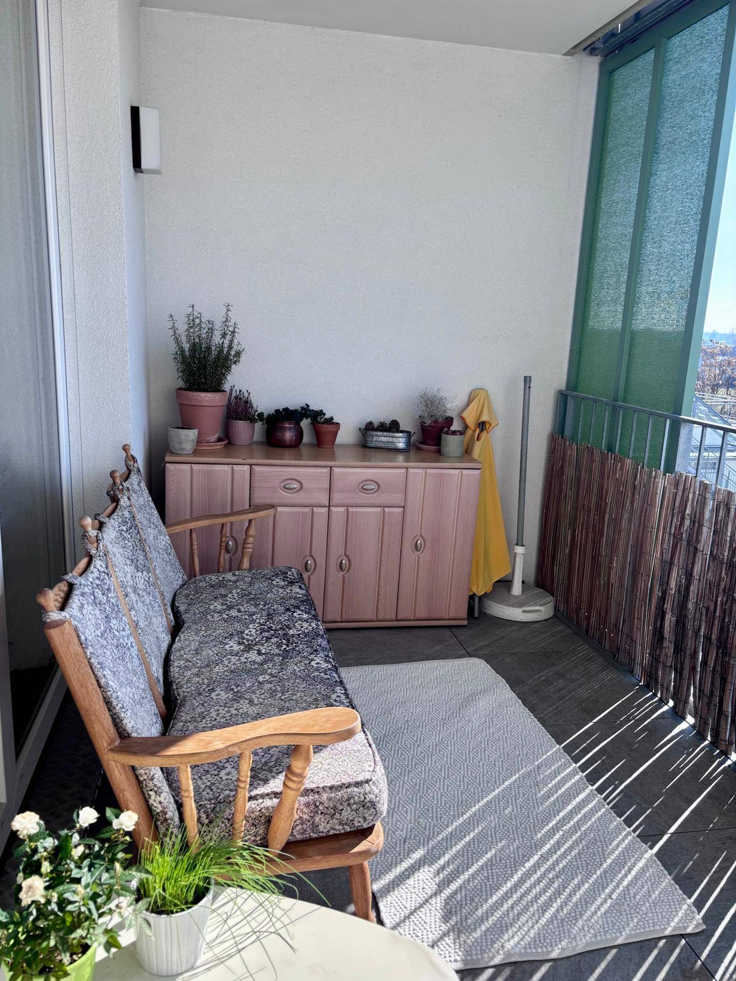 Gemütlicher Balkon mit Holzbank, Pflanzen und einem sonnigen Platz zum Entspannen.
