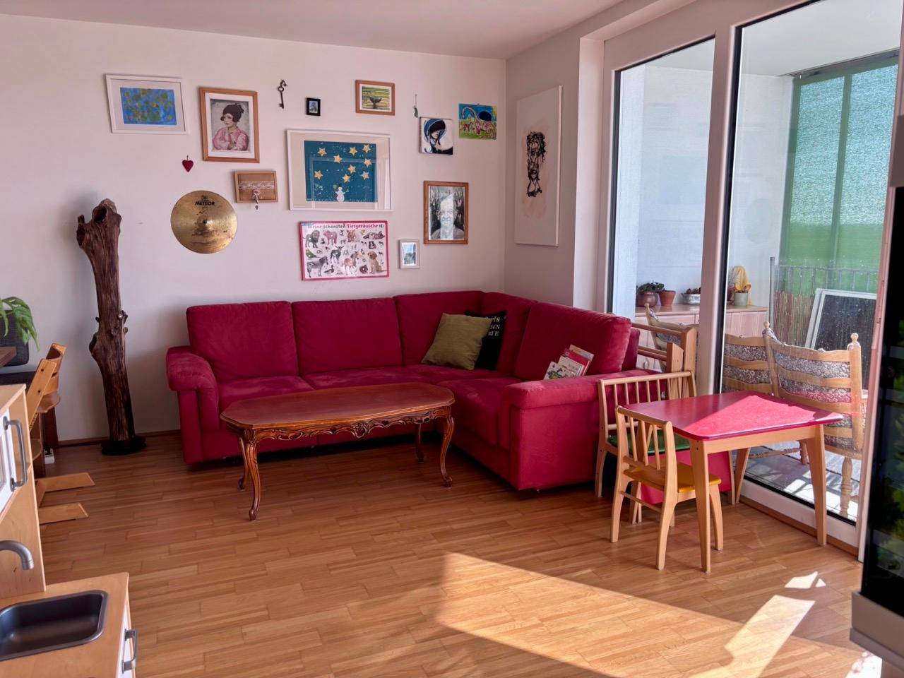 Gemütliches Wohnzimmer mit rotem Ecksofa, Holzboden und einer Spielecke für Kinder.