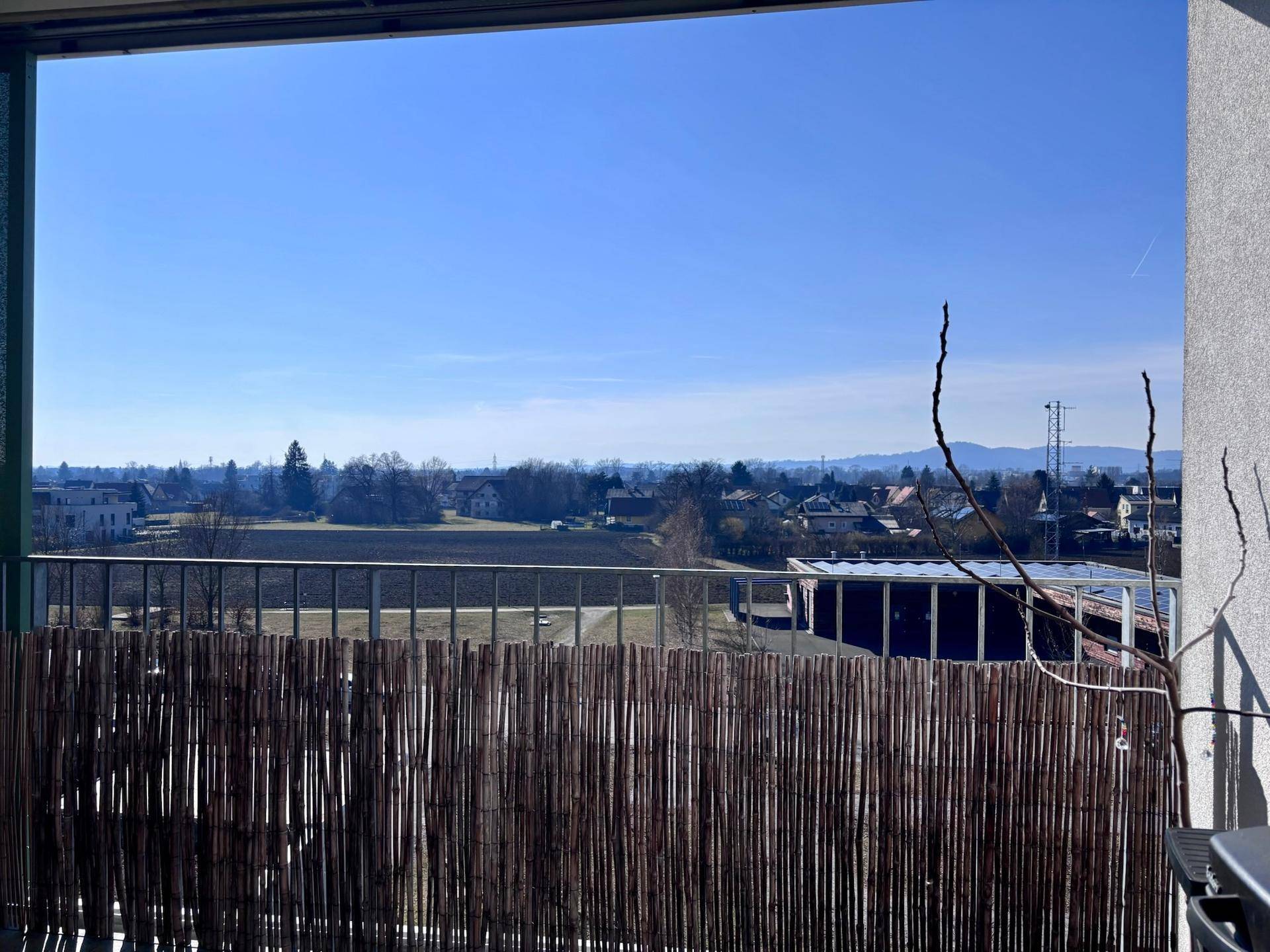 Weitblick vom Balkon über Felder, Häuser und die umliegende Berglandschaft.