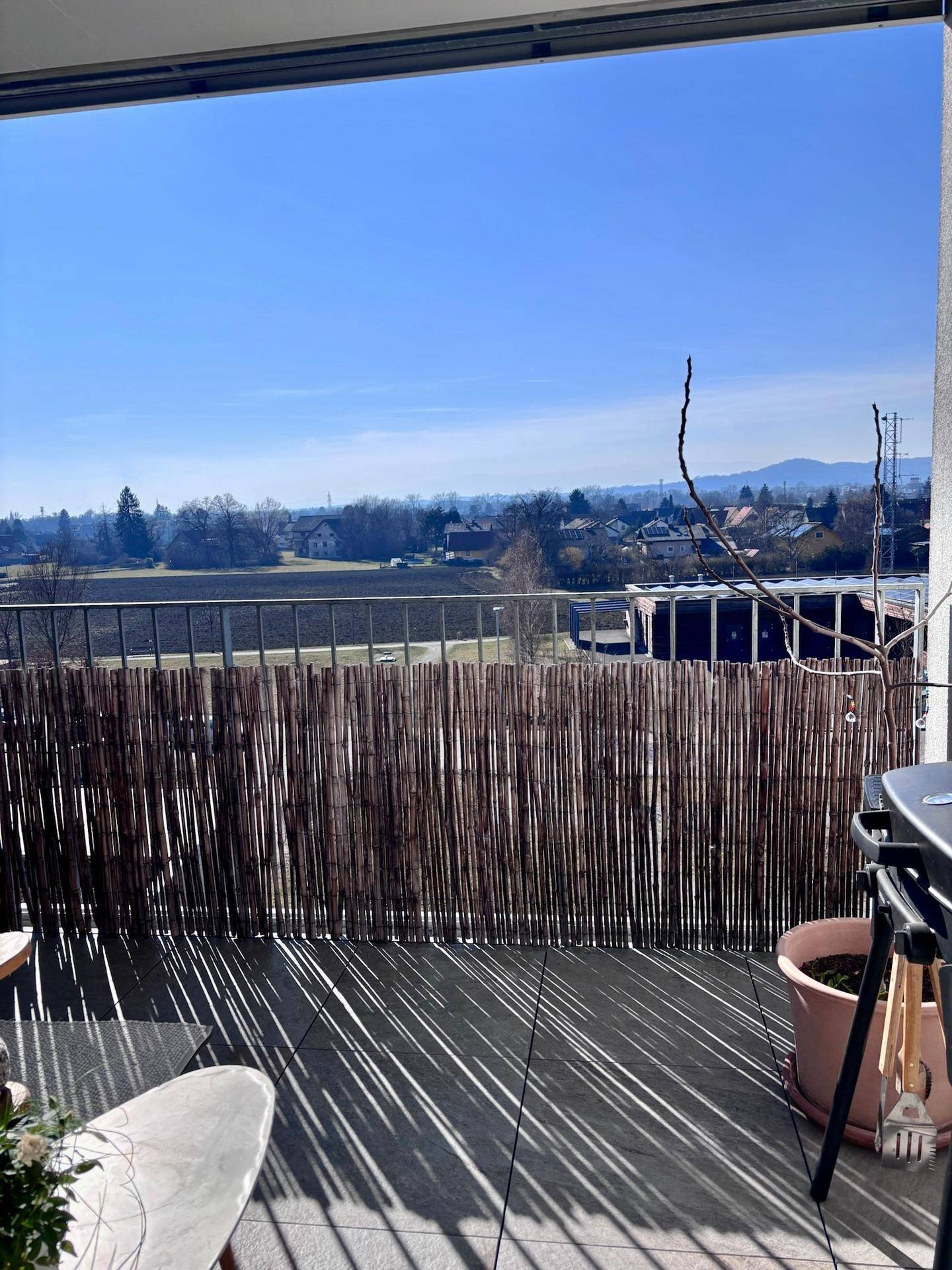 Geräumiger Balkon mit Fliesenboden, Grill und sonnigem Ausblick ins Grüne.