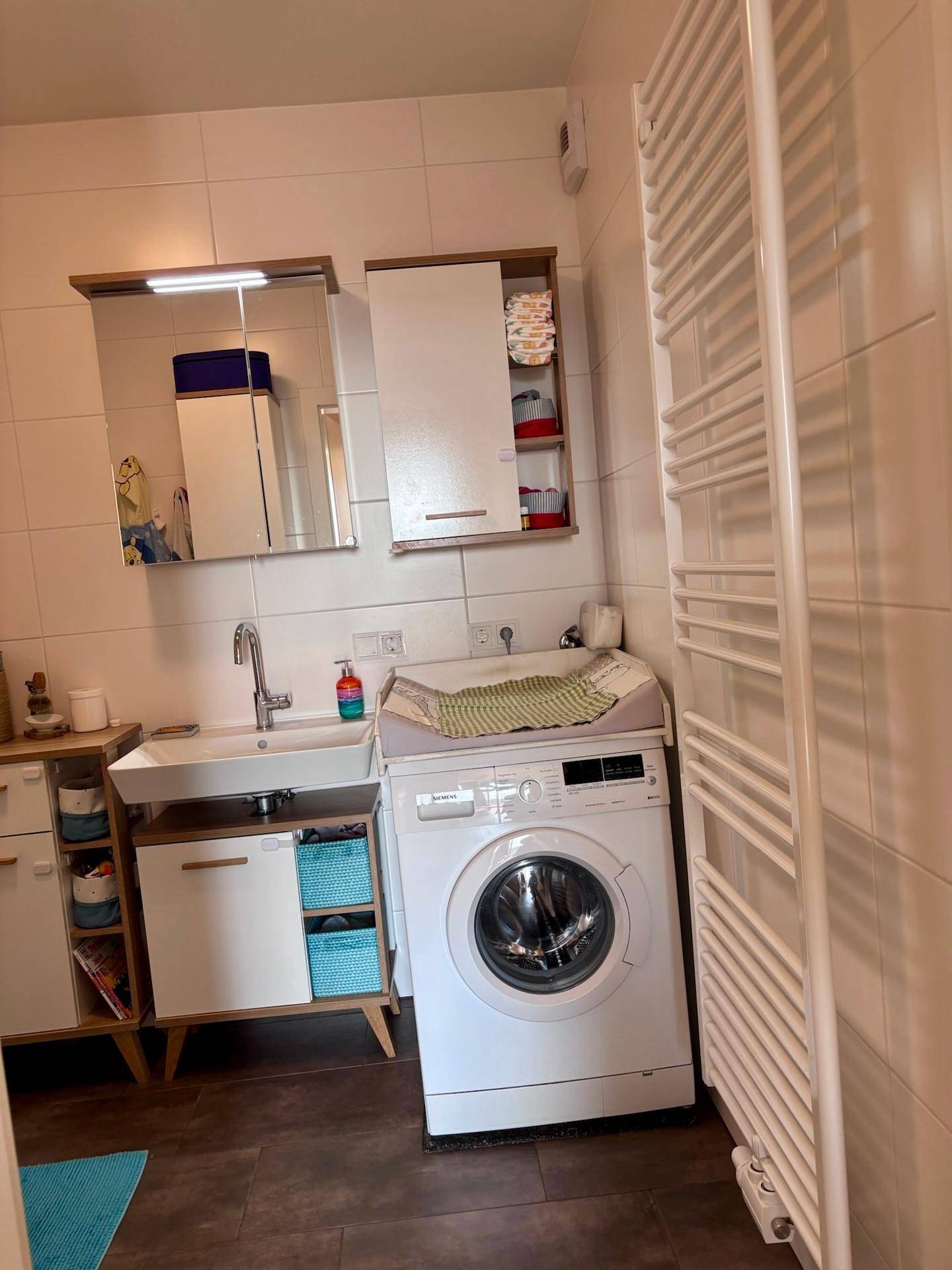 Badezimmer mit Waschbecken, Spiegelschrank, Waschmaschine und beheiztem Handtuchhalter.