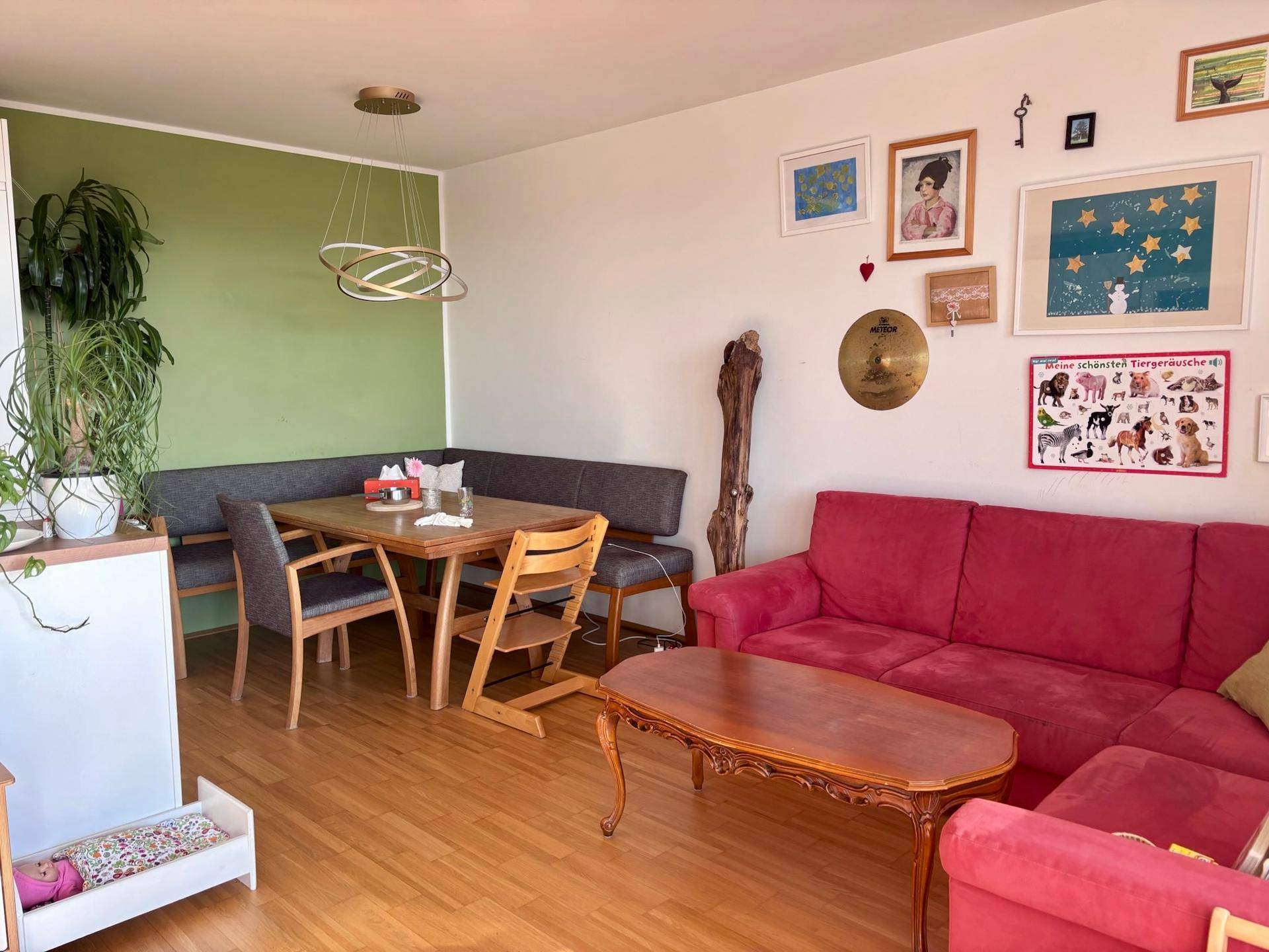 Offener Wohn- und Essbereich mit rotem Sofa, Esstisch und grüner Akzentwand.
