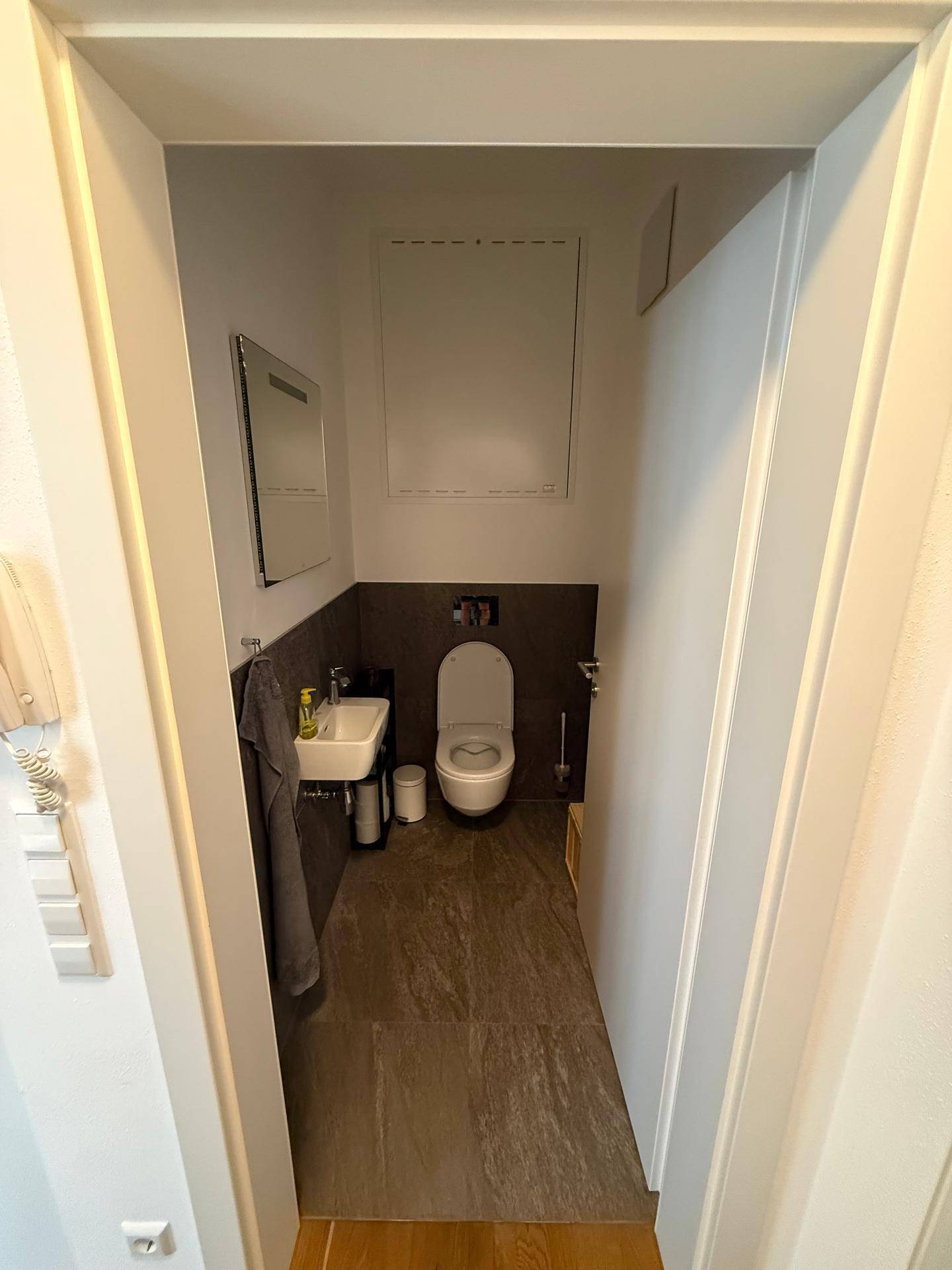 Modernes Gäste-WC mit dunklen Fliesen, wandhängender Toilette und kleinem Waschbecken.