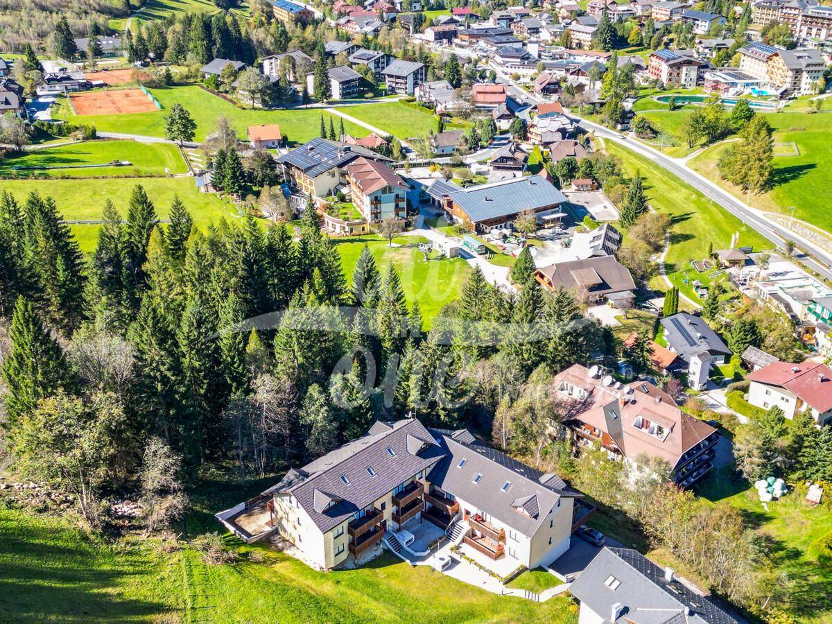 Weitläufige Luftaufnahme eines Wohnkomplexes in einer grünen Bergregion mit angrenzendem Dorf.