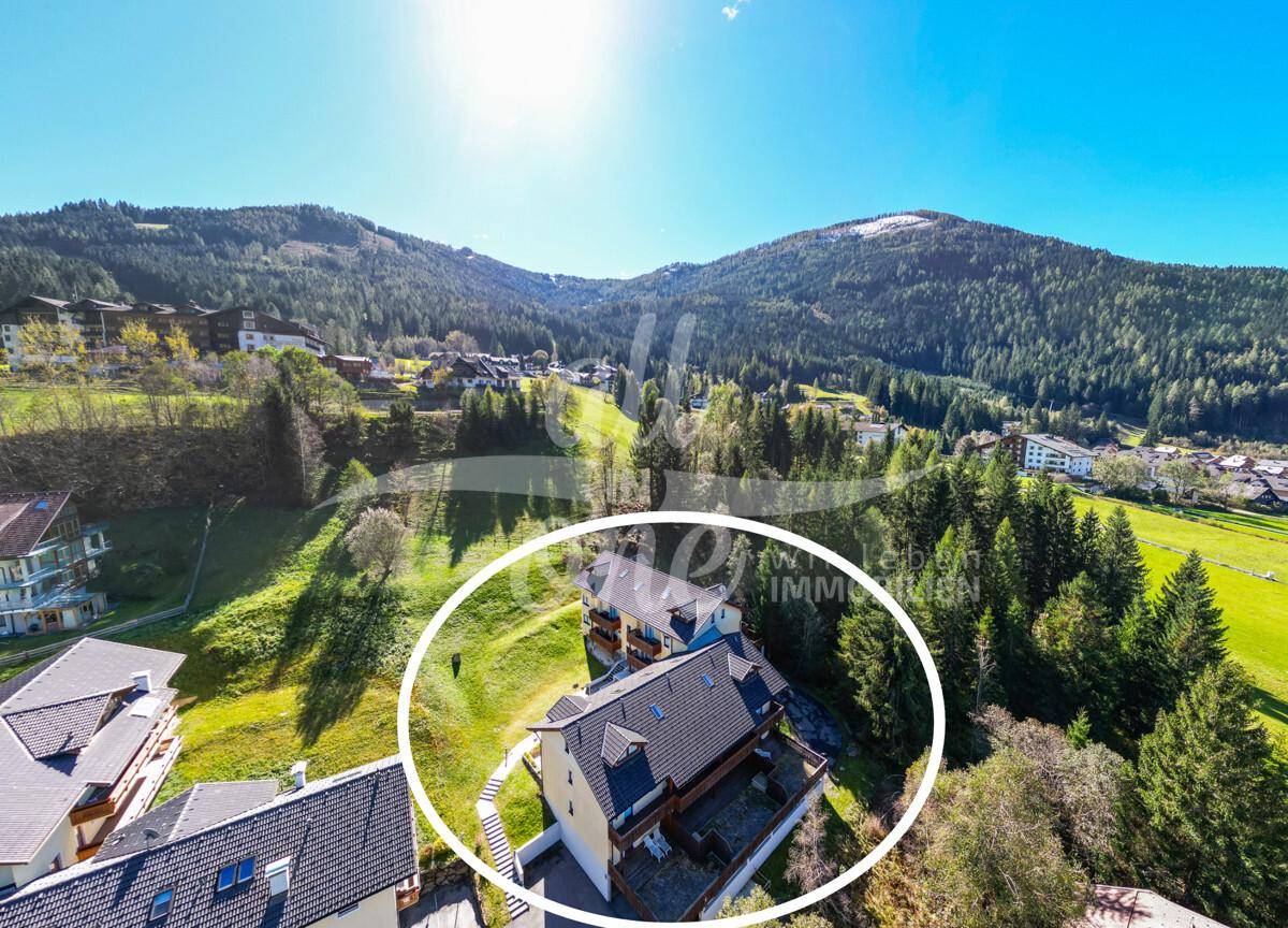 Luftaufnahme eines Anwesens in einer grünen Berglandschaft unter strahlend blauem Himmel.