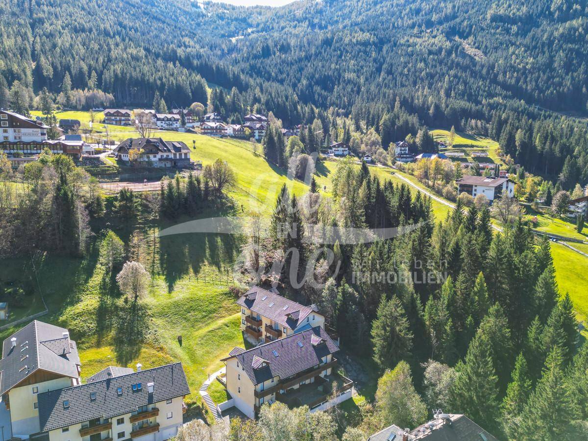 Luftaufnahme des Wohnkomplexes mit dem Dorf und den bewaldeten Bergen im Hintergrund.