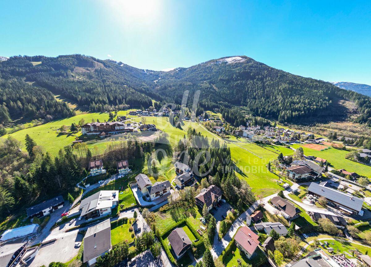Weitläufige Luftaufnahme des gesamten Dorfes und der umliegenden alpinen Berglandschaft.