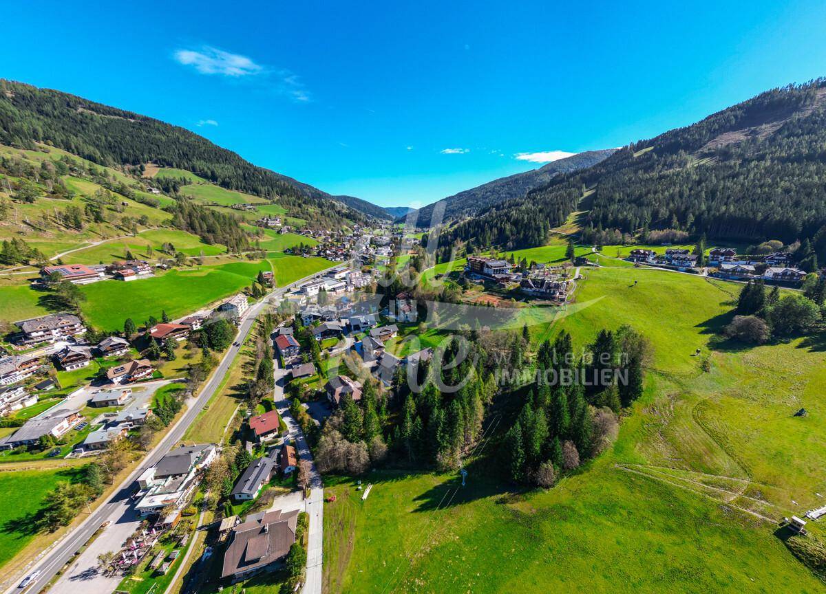 Panoramablick aus der Luft auf das Tal mit dem Dorf, der Straße und den bewaldeten Bergen.