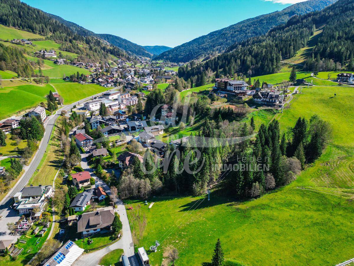 Weitläufige Luftaufnahme des Tals mit dem Dorf, der Straße und den umliegenden Bergen.