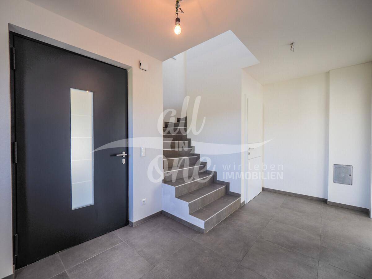 Moderner Eingangsbereich mit dunkler Haustür, Treppe und hellem Fliesenboden.