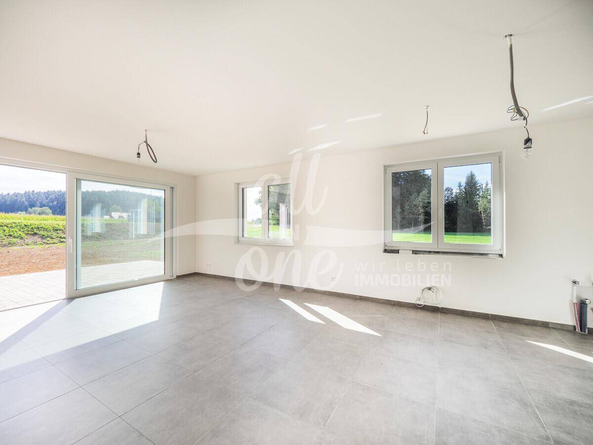 Geräumiges Wohnzimmer mit großen Schiebetüren, Fliesenboden und weitem Blick ins Grüne.