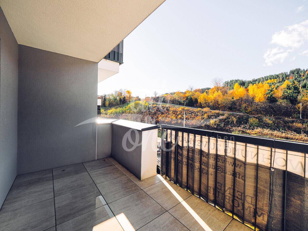 Sonniger Balkon mit Fliesenboden und weitem Blick auf herbstliche Bäume und Landschaft.