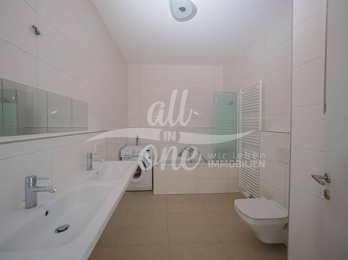 Modernes Badezimmer mit weißen Fliesen, Doppelwaschbecken, Dusche und Waschmaschine.